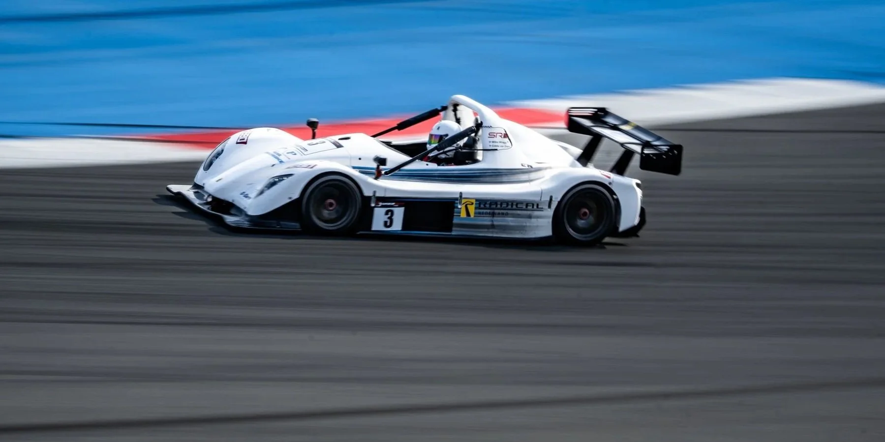 A white race car with the number 3 on the side speeding on a racetrack, blurred background indicating high speed.