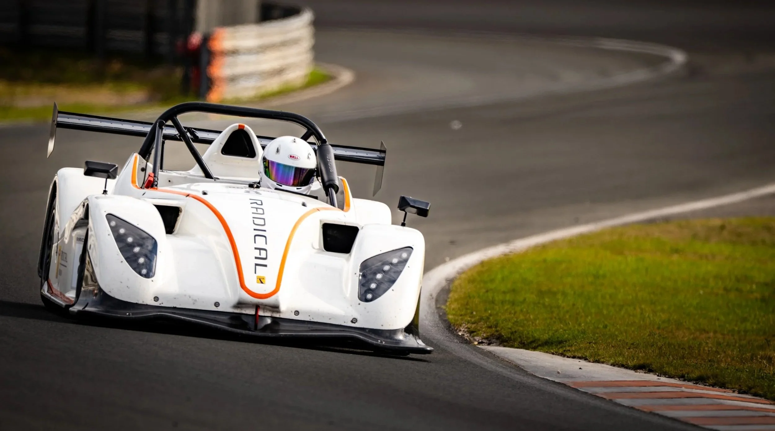 A white race car with orange accents navigating a curve on a race track.