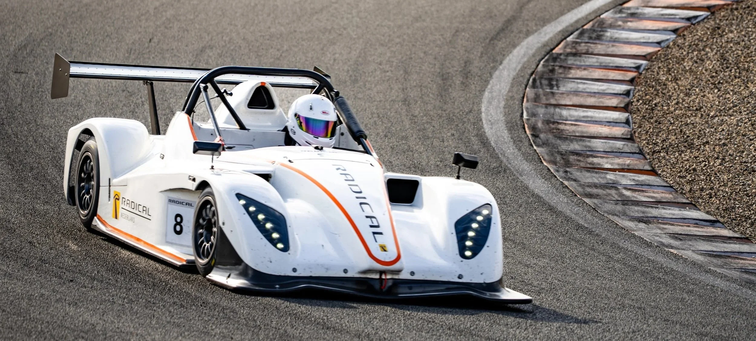 A white race car with the number 8 and sponsor logos is speeding along a racetrack, taking a corner with visible tire marks on the asphalt.