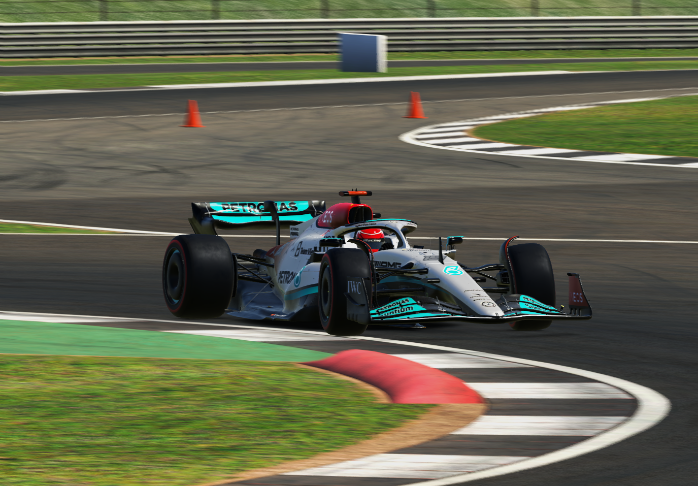 A Formula 1 race car on a racing track, navigating a curve with orange traffic cones, with barriers and grassy areas in the background.
