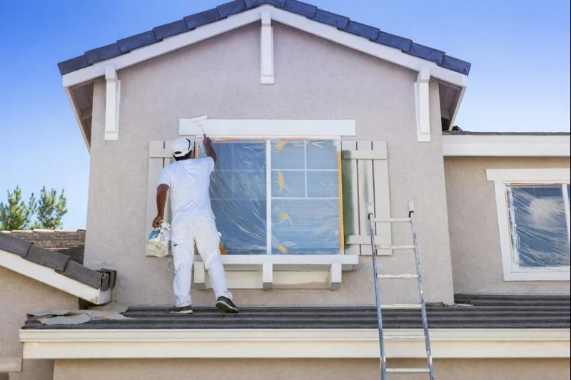 A painter painting the exterior window frame of a house during daytime.