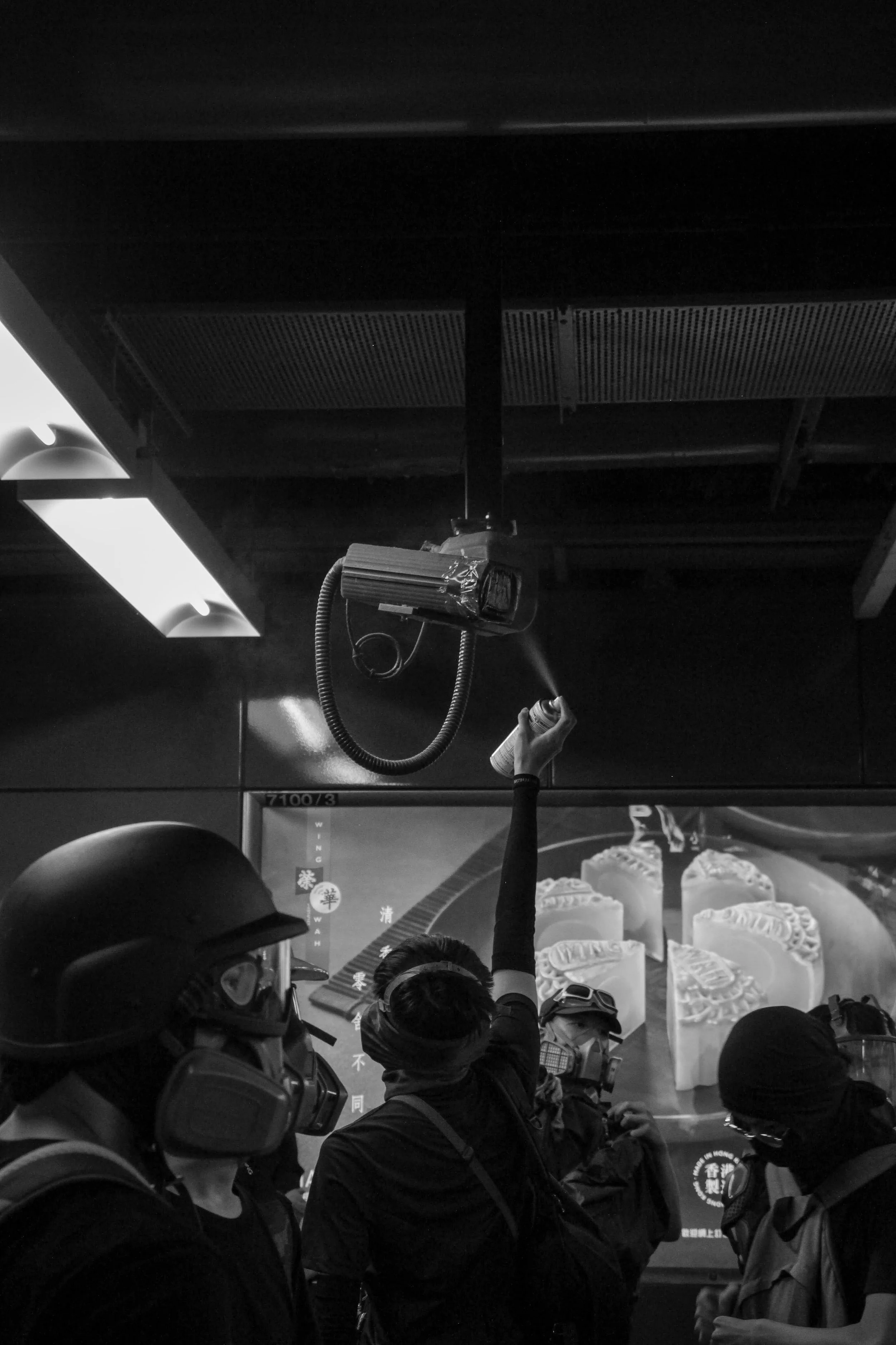 Group of police officers and individuals in a crowded indoor setting, with some holding items, and posters or advertisements in the background.