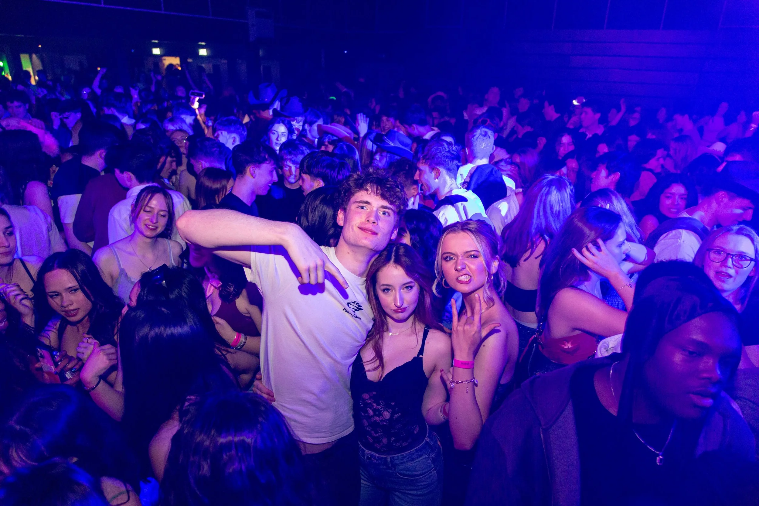 A large crowded dance floor at a nightclub with people dancing and enjoying the music, illuminated by purple and blue lighting.