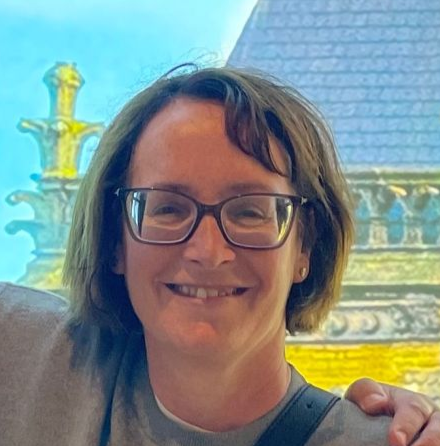 Smiling woman with glasses in front of a fountain and a steeple building.