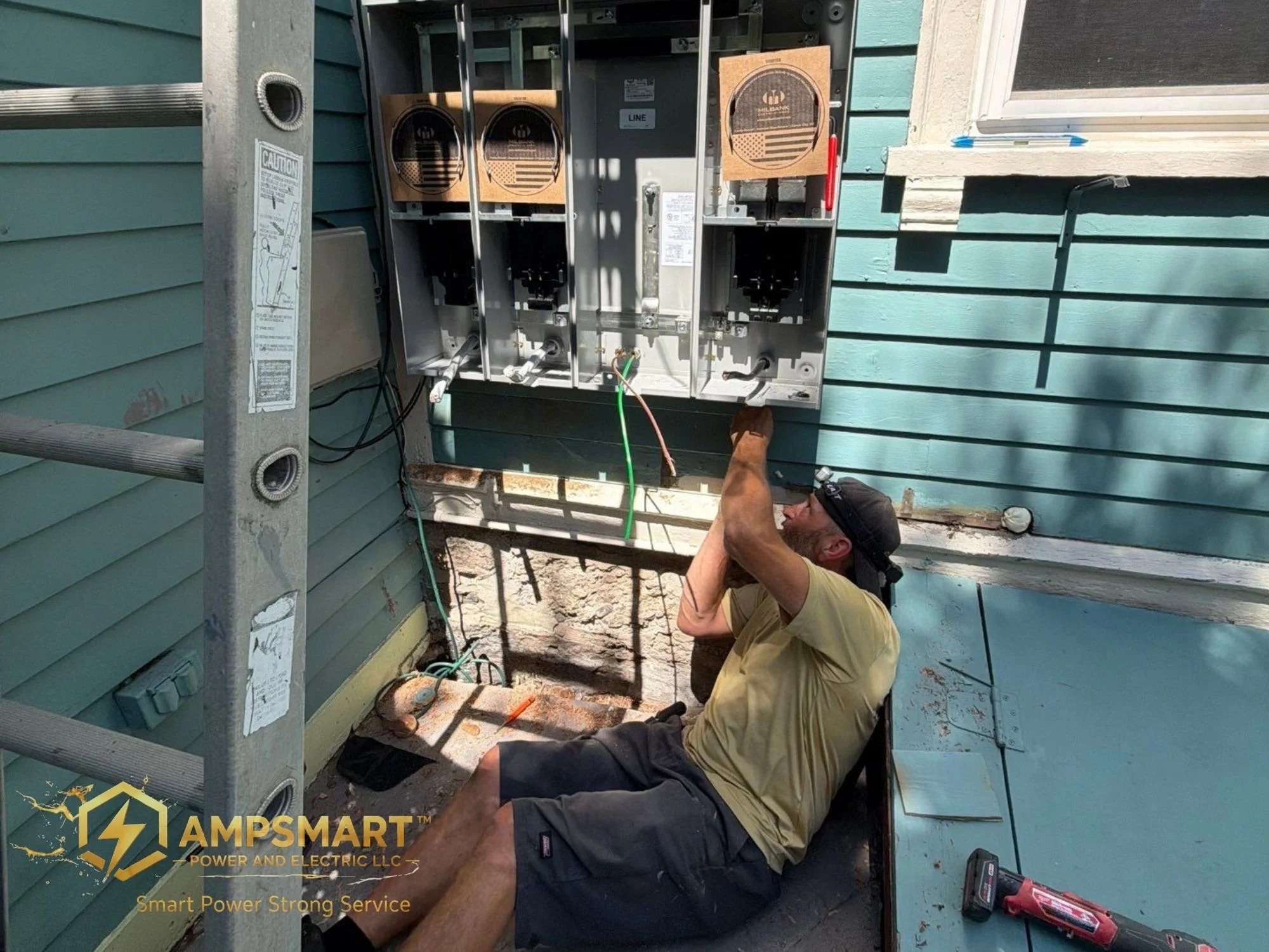 A technician working on an electrical panel outside a house with teal siding, with tools and wires visible around him.