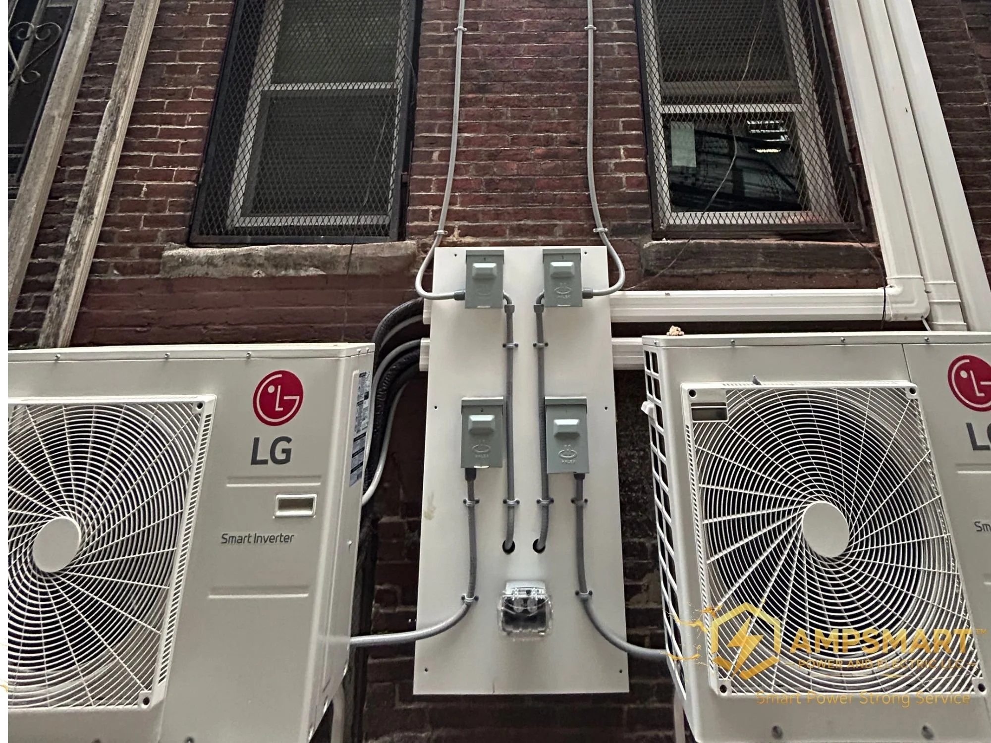 Exterior view of an HVAC system mounted on a brick wall, with two LG branded air conditioning units and electrical wiring connected between them.