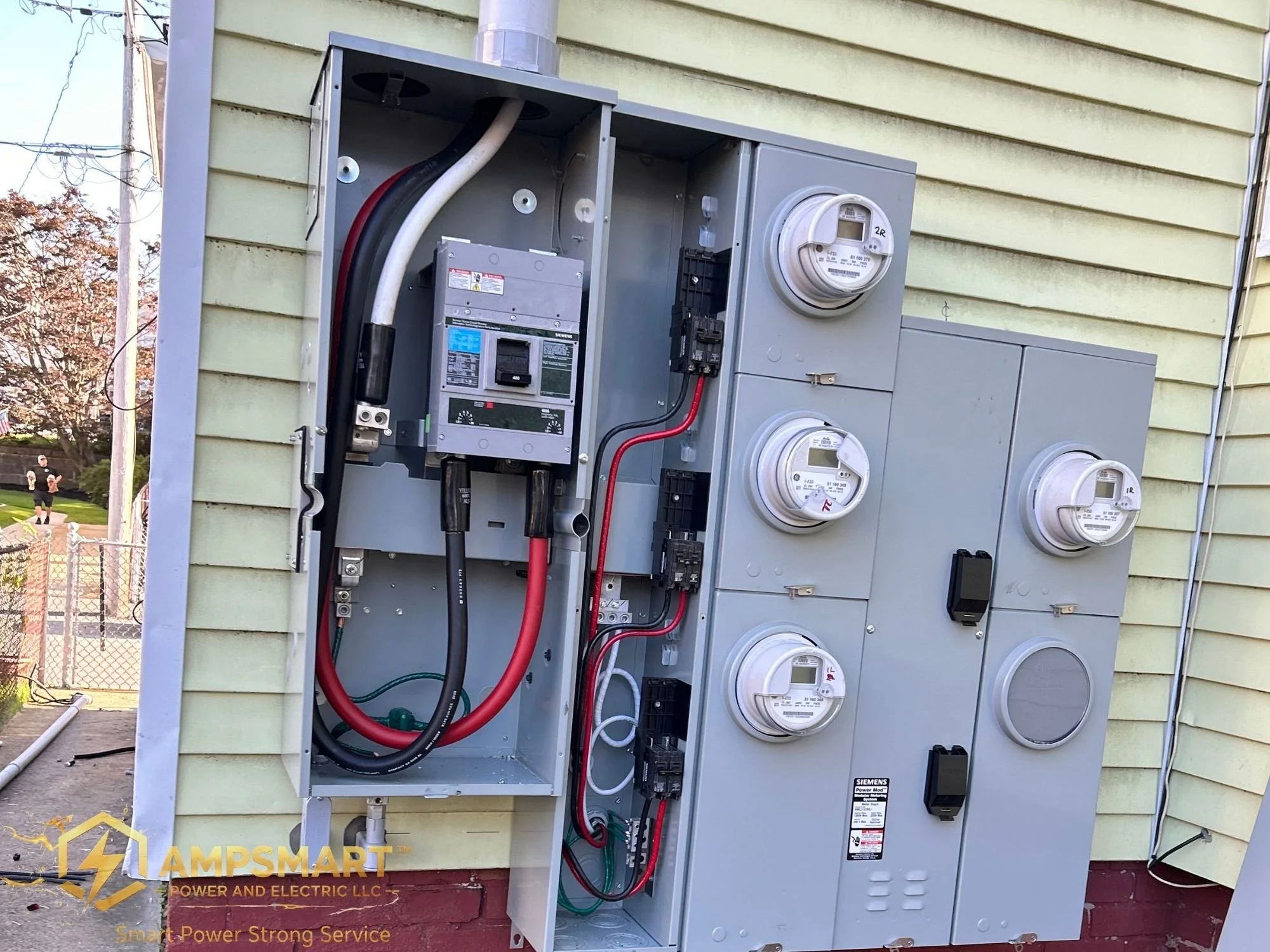 An electrical meter panel with several circuit breakers and meters installed on the exterior of a house with light yellow siding.