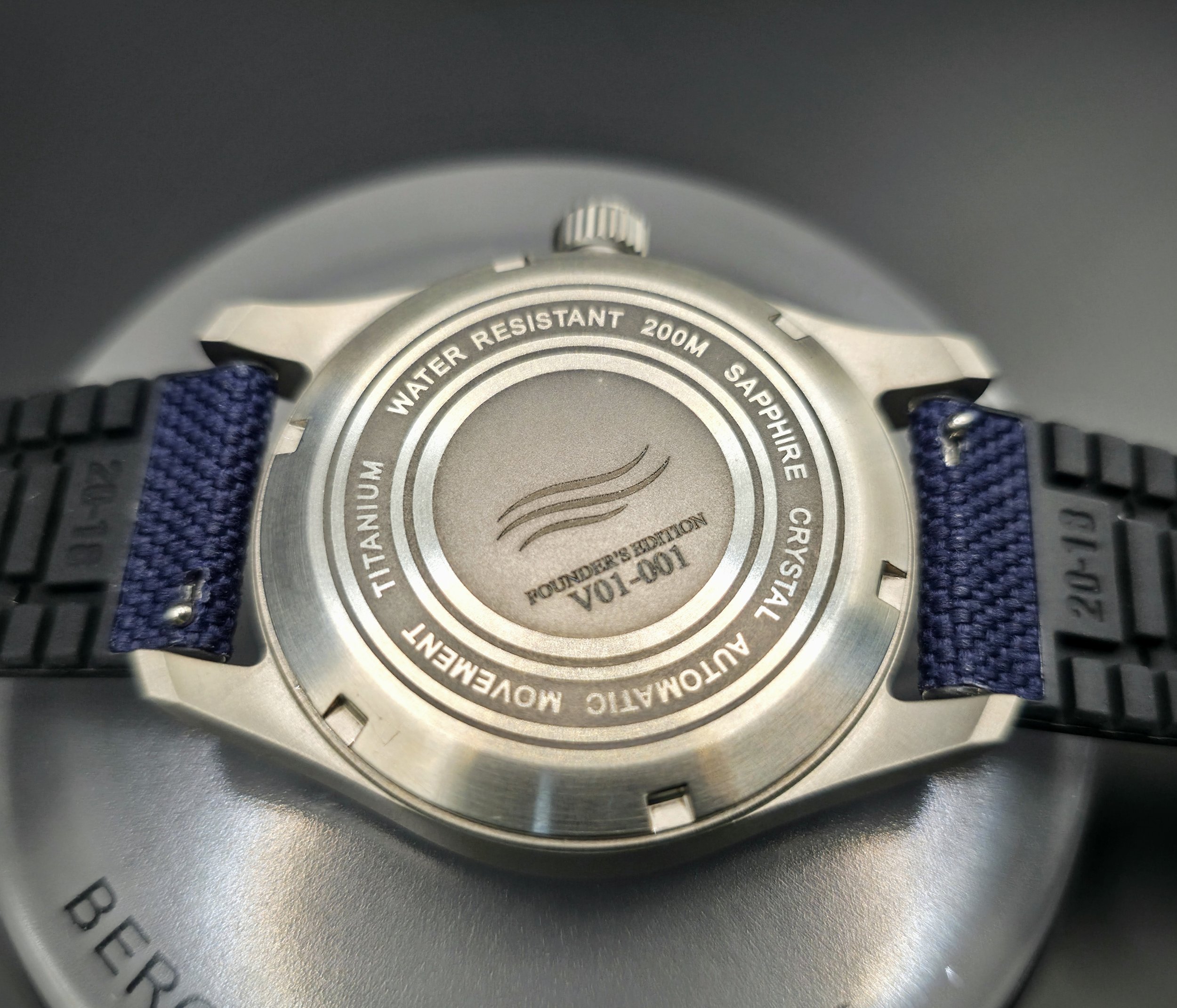 Vanguard field watch case back engraved with logo and founder's edition 001. Titanium case, automatic movement, sapphire crystal, 200m water resistance, blue sailcloth rubber strap, 20mm lug width, screw down crown.