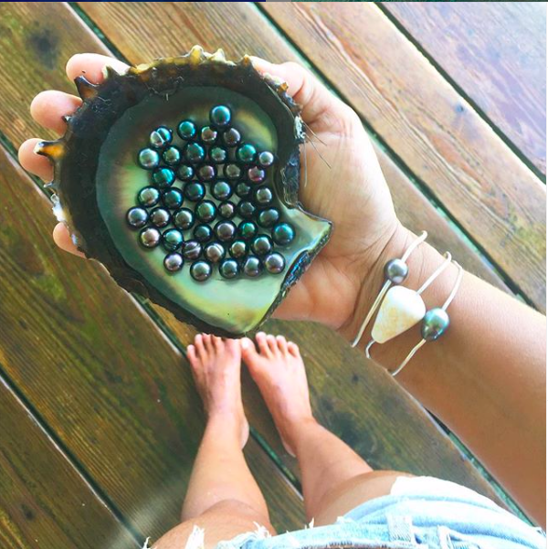 A hand holding an large oyster shell full of black pearls in Tahiti