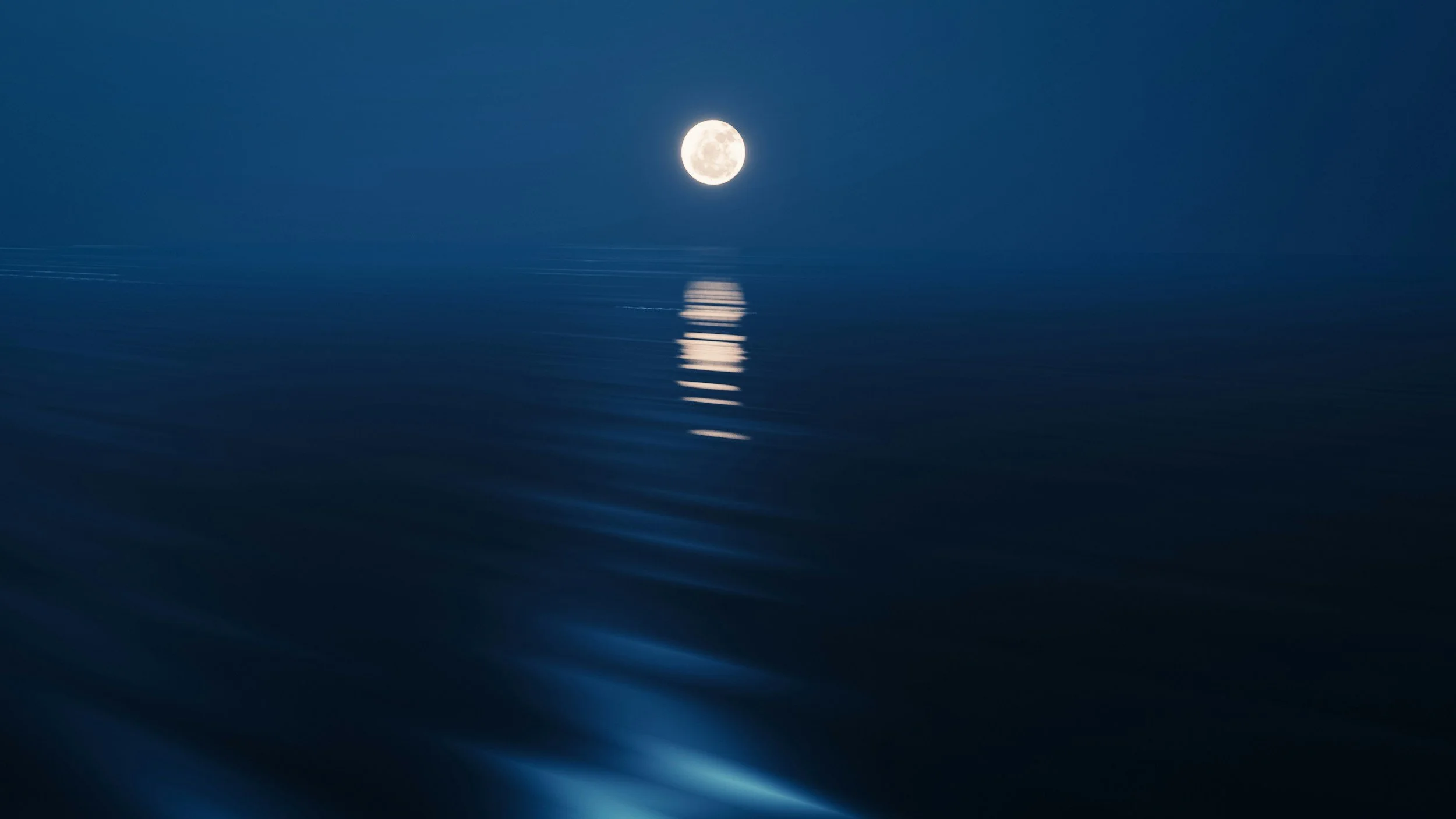 Full moon over calm ocean waters, reflecting the moon's glow on the surface.