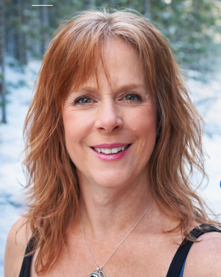 A woman with red hair smiling outdoors with trees and snow in the background.