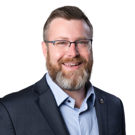 A smiling man with glasses, a beard, and short hair, wearing a dark suit jacket and a light blue collared shirt.