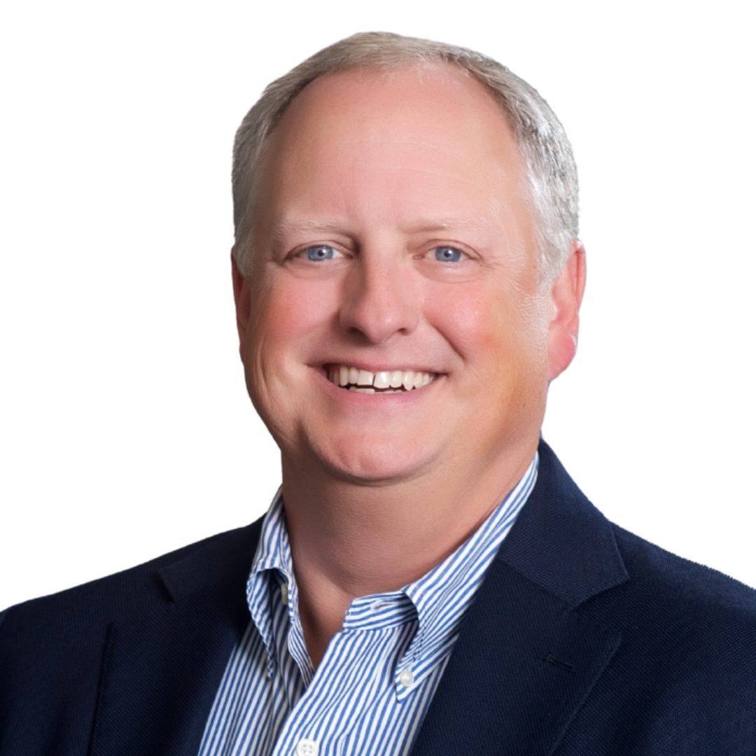 Headshot of a smiling middle-aged man with short blond hair, blue eyes, in a navy blazer and striped dress shirt against a white background.