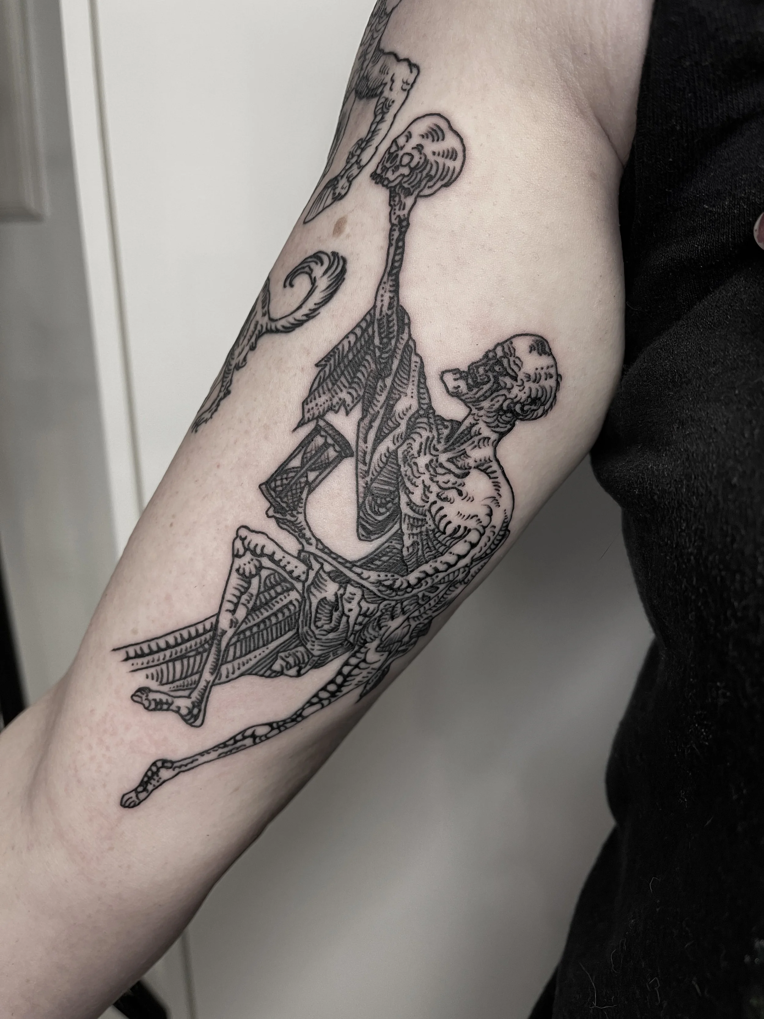 Schwarz-weiß-Tattoo eines Skeletts mit Flügeln auf dem Oberarm.