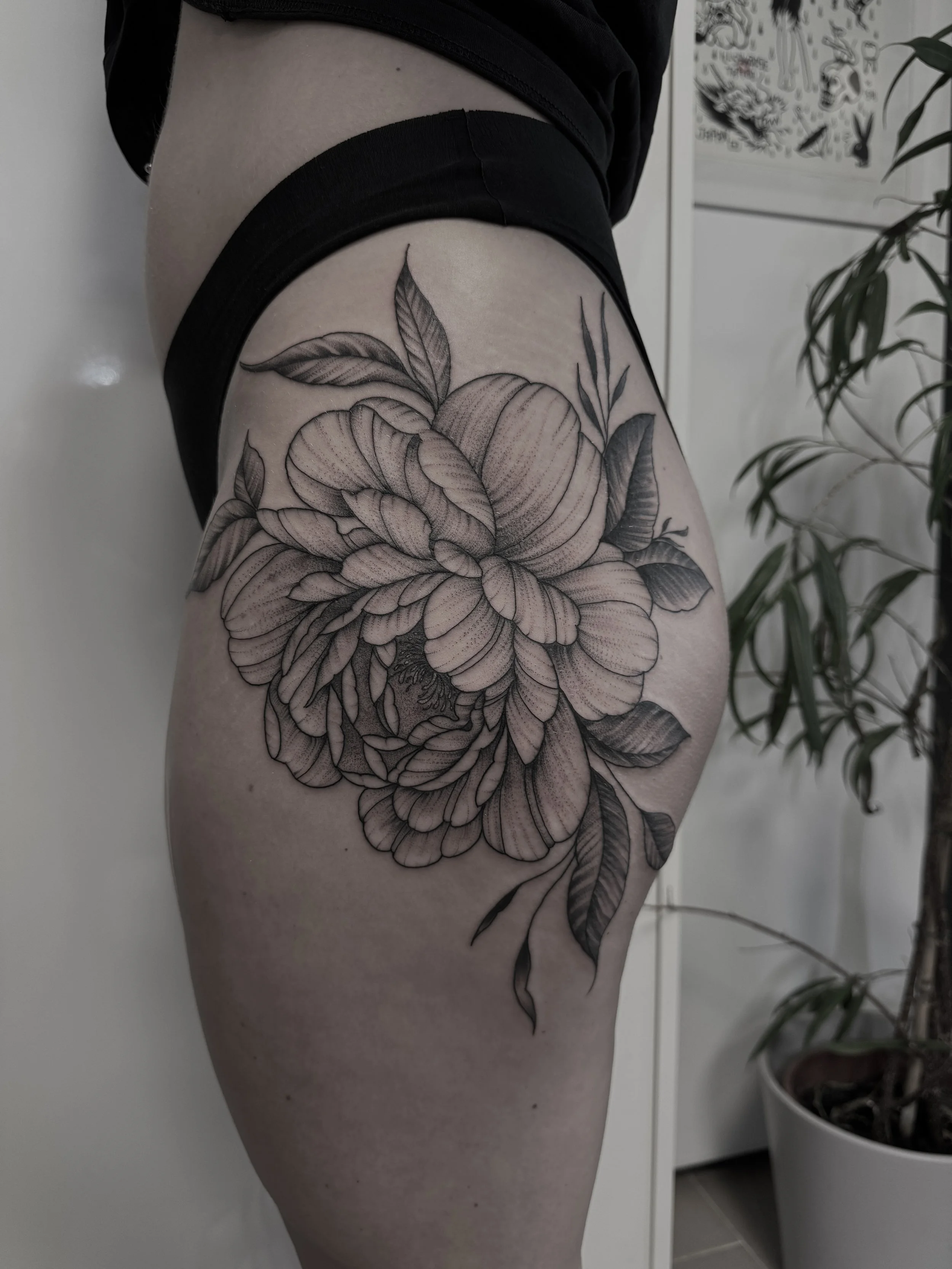 Schwarz-weiß Tattoo einer großen, detaillierten Blume mit Blättern am Oberschenkel einer Person.