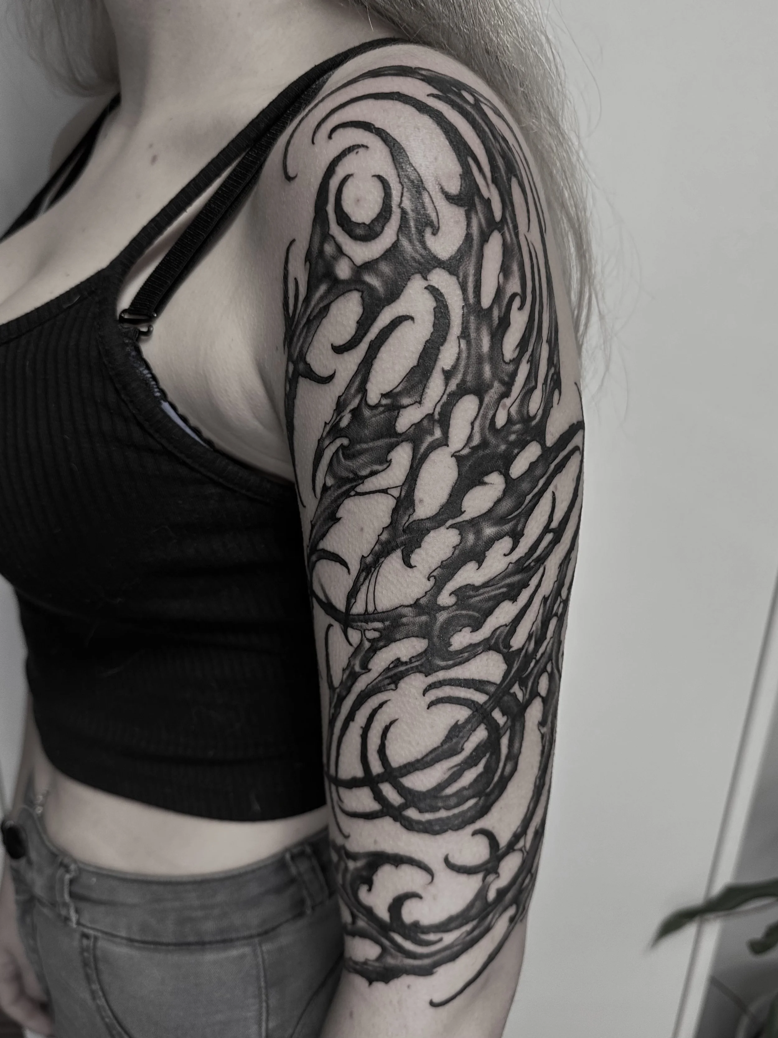 Schwarzes Tribal-Tattoo auf dem Oberarm einer Person.