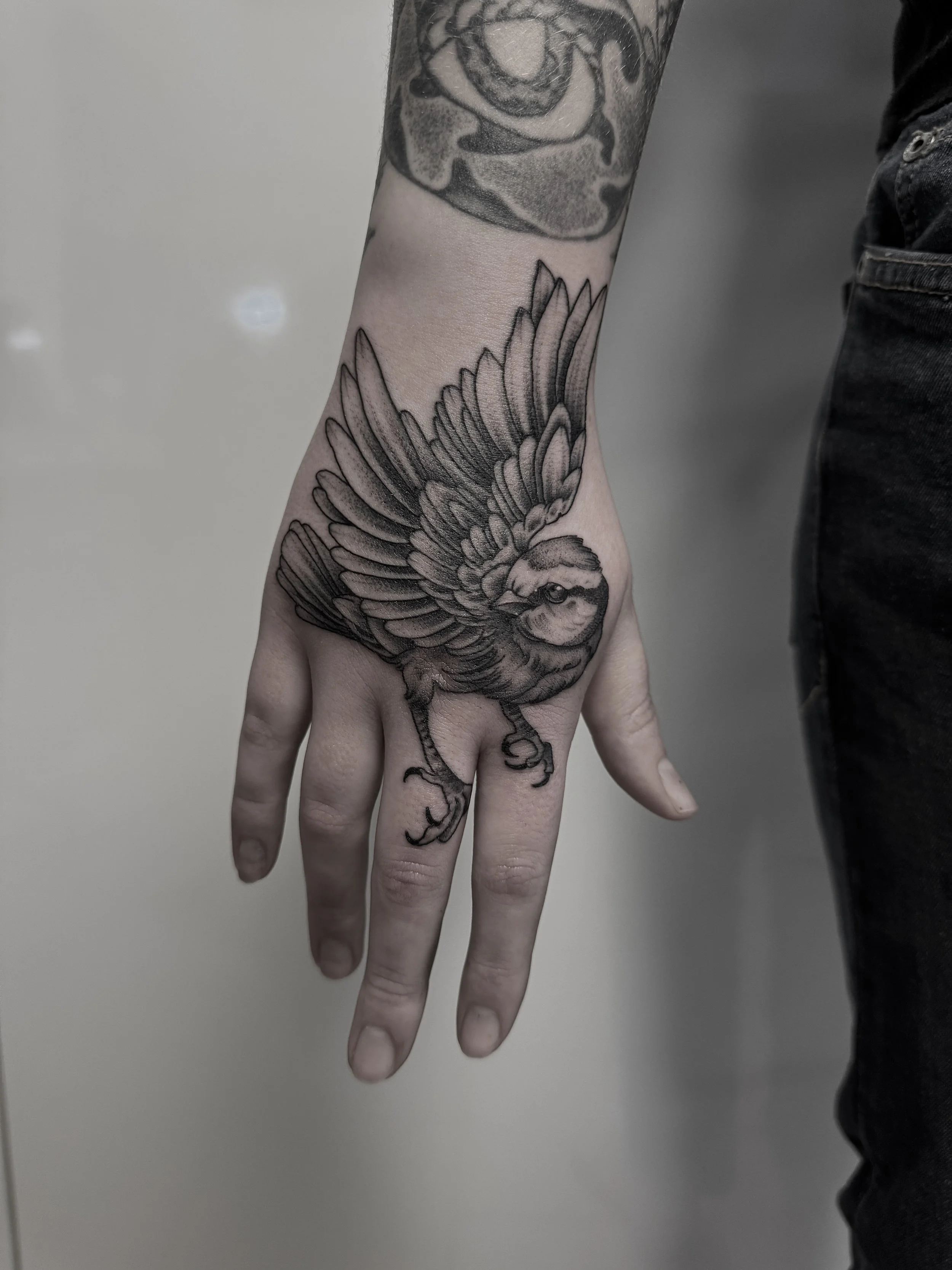 Schwarze Tätowierung einer fliegenden Vogel auf der Hand.