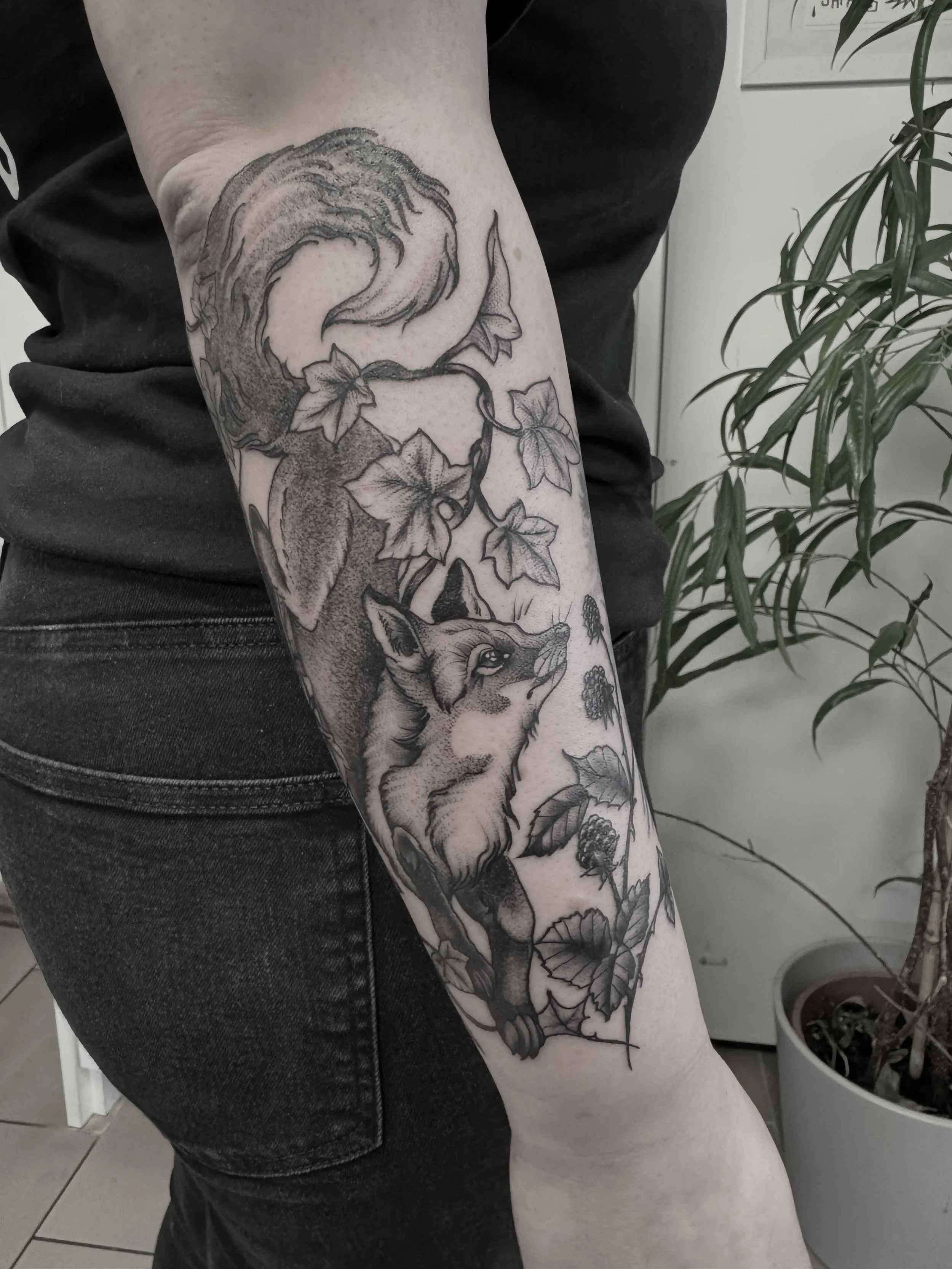 Detailliertes schwarzes Tattoo eines Fuchses, umgeben von Blättern und Heckenrosen auf dem Unterarm.