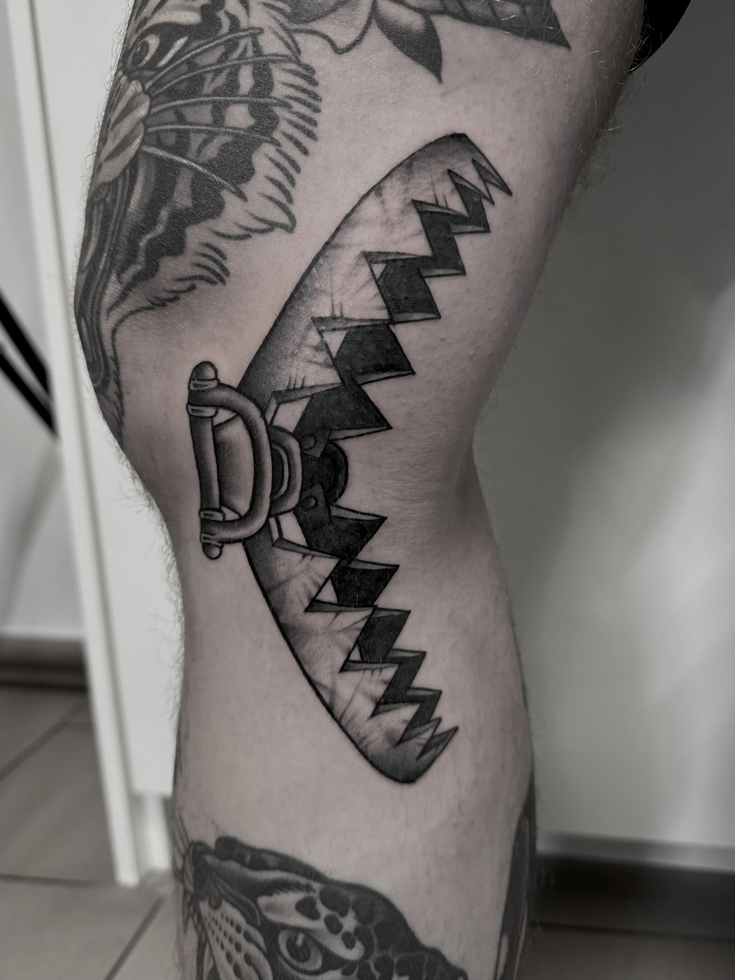 Tattoo eines Kettensägenschwerts auf dem Oberarm, schwarz-weißer Realismusstil.