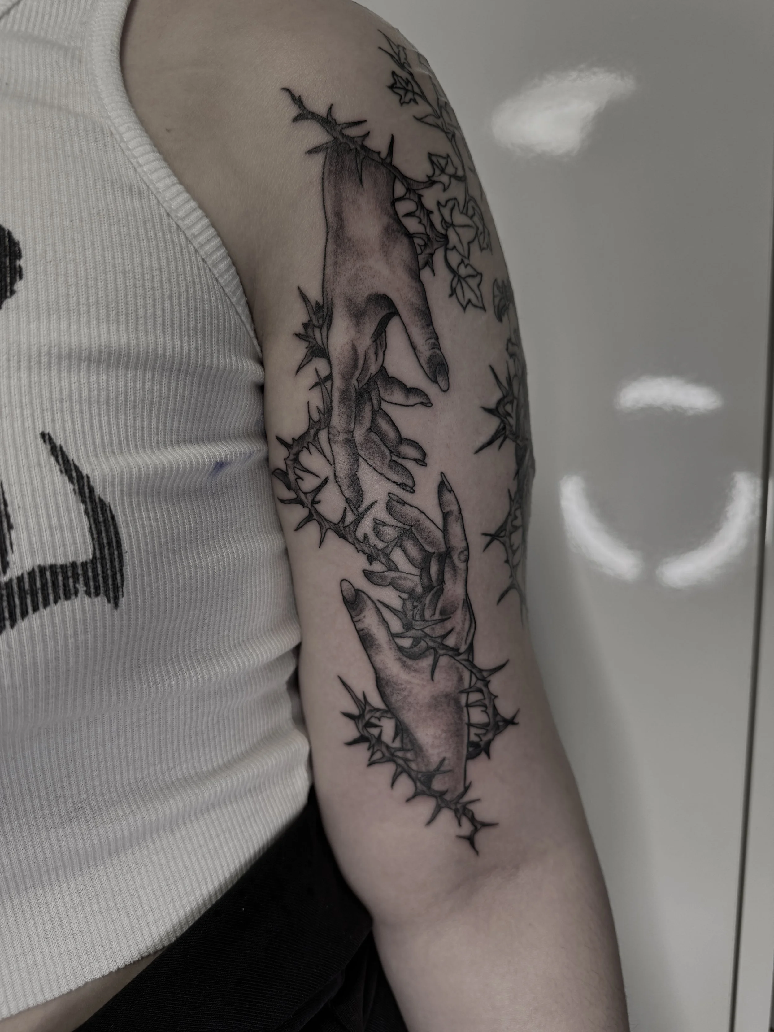 Tattoo von zwei Händen, die sich berühren und von Dornen umgeben sind, auf dem Oberarm.