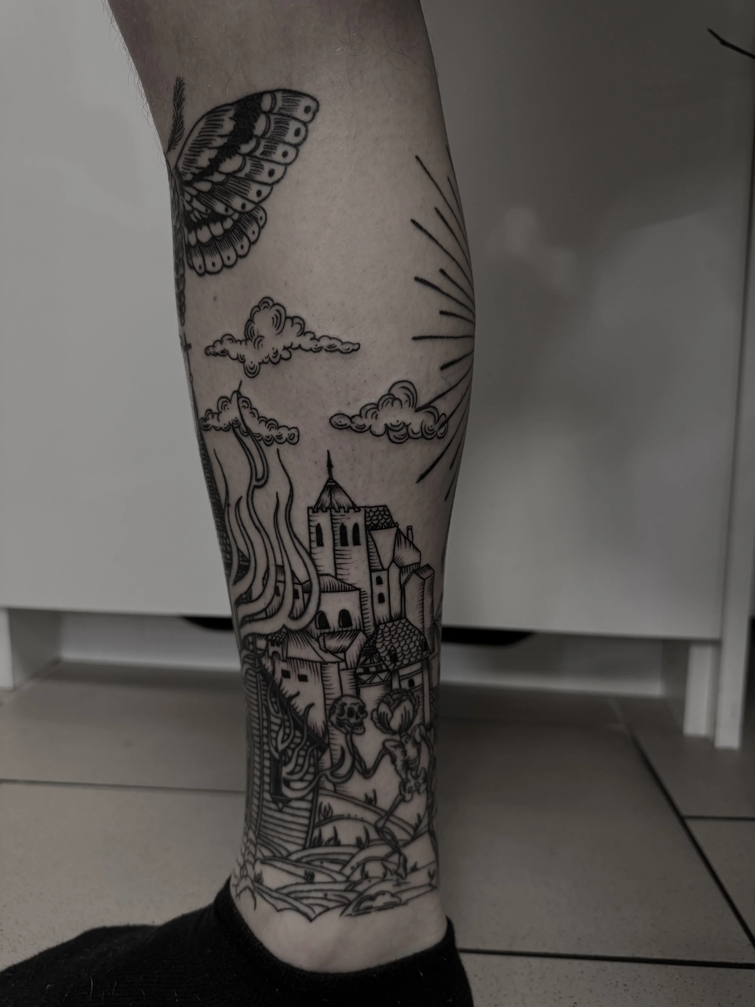 Schwarz-weiße Tätowierung eines Hügellands mit Häusern, Wolken, Sonne, Schmetterling und einer Frau mit langem Haar auf dem Bein.