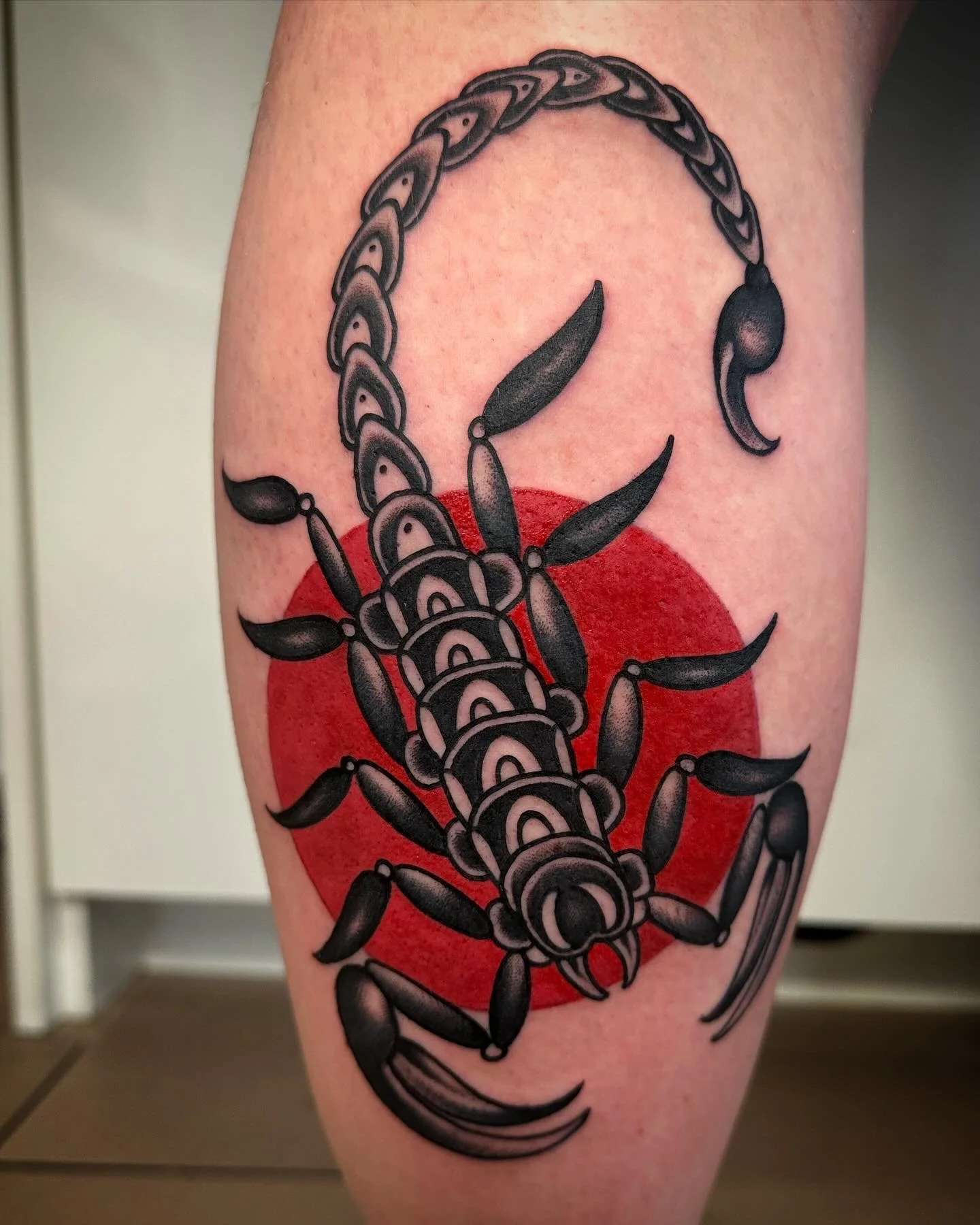 Tattoo eines Skorpion mit rotem Kreis im Hintergrund.