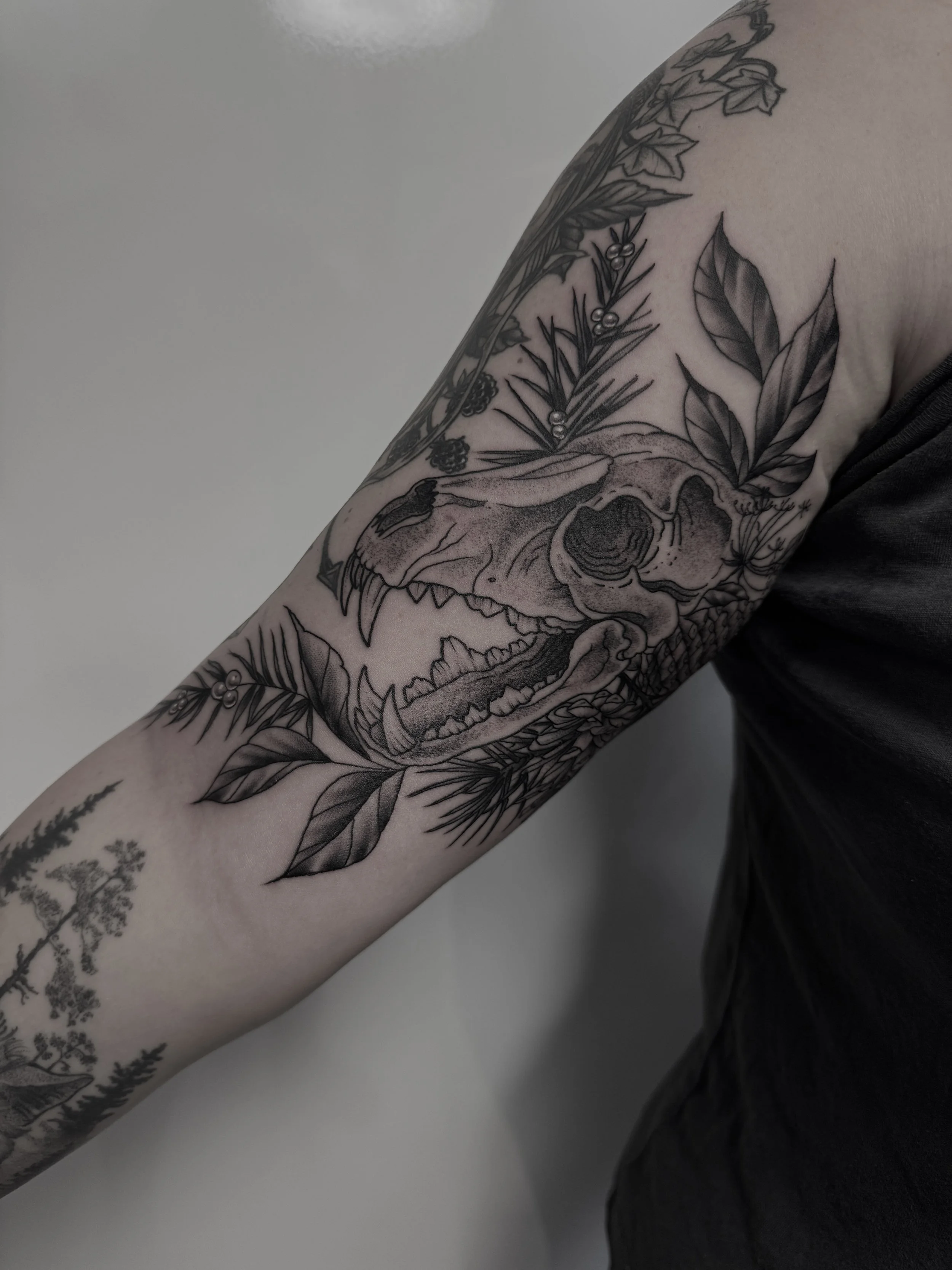 Schwarze Tätowierung eines Tier-Schädels mit umgebenden Blättern auf dem Oberarm