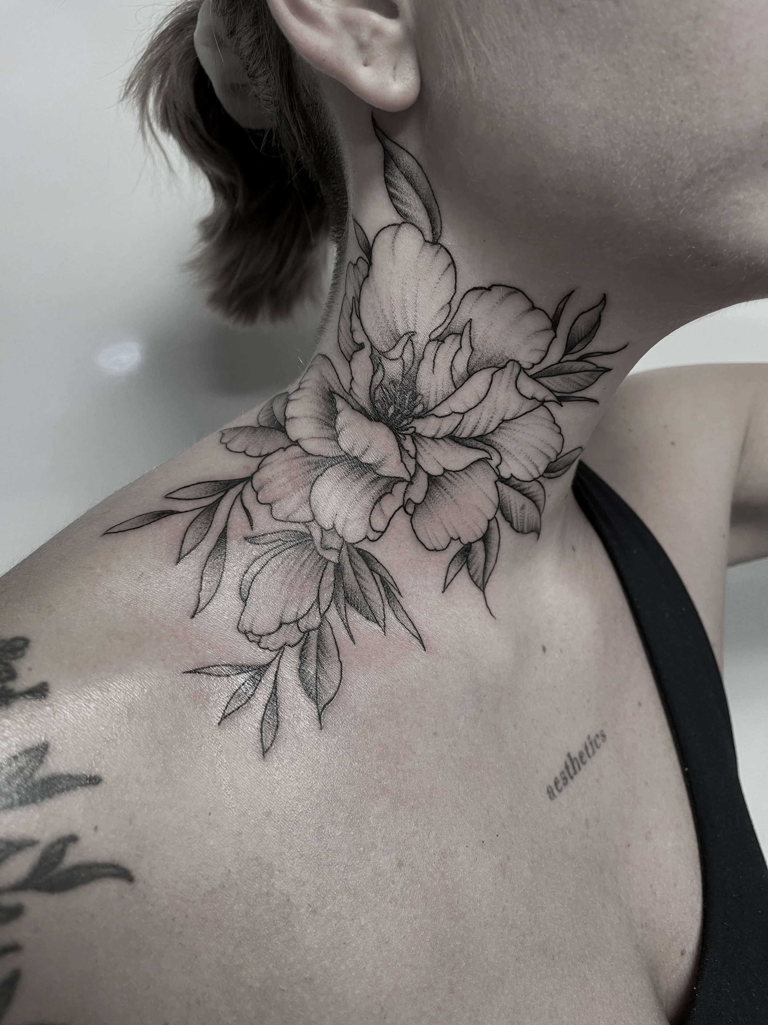 Nahaufnahme eines schwarzen Tattoos eines großen Blumenmusters am Hals und Schulter einer Person.