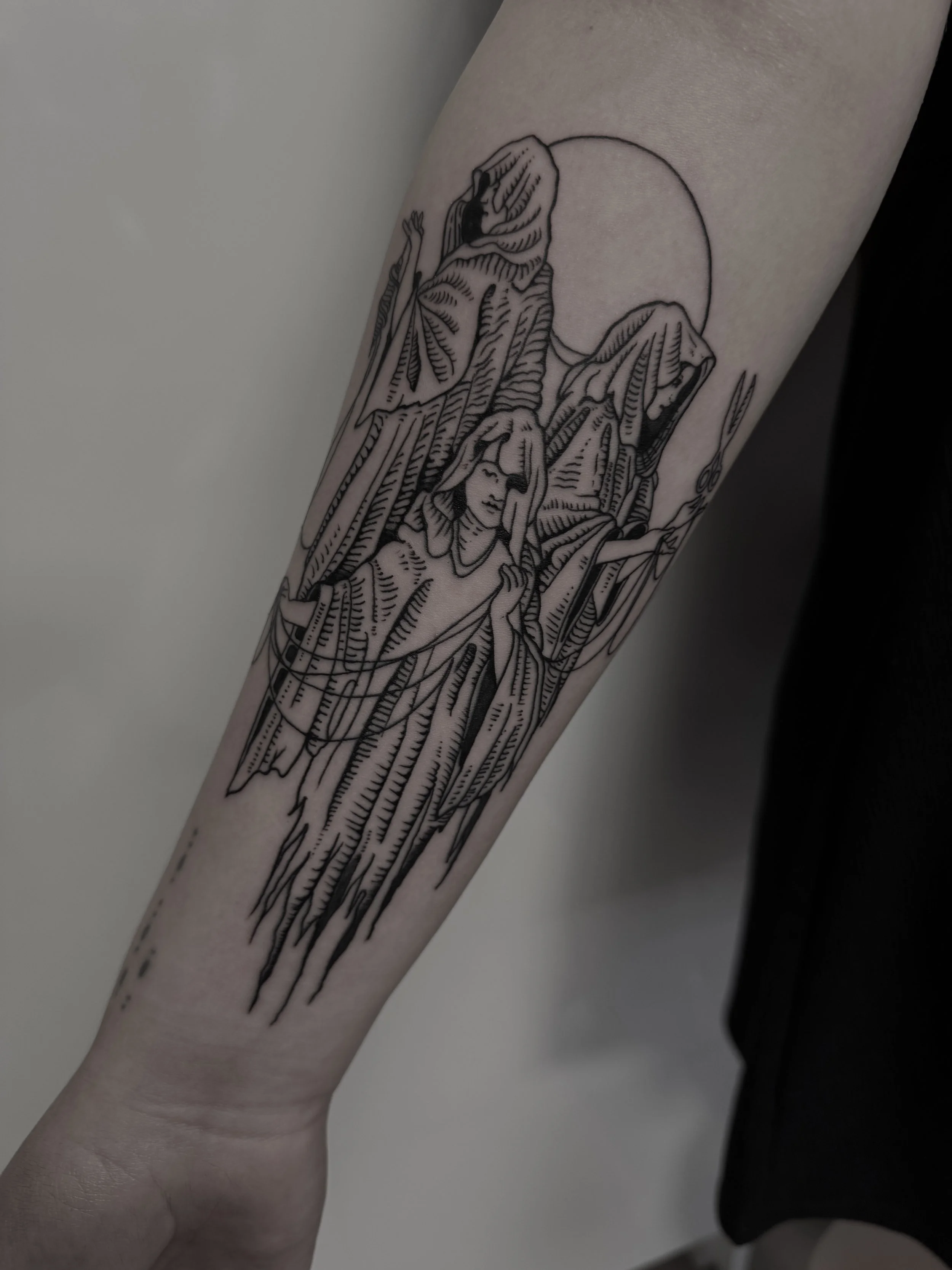 Schwarze Linien-Tattoo auf dem Unterarm zeigt Figuren, die wie Frauen mit langen Haaren und hängenden Kleidern erscheinen, vor einem Kreis. Das Design ist stilisiert und geometrisch.