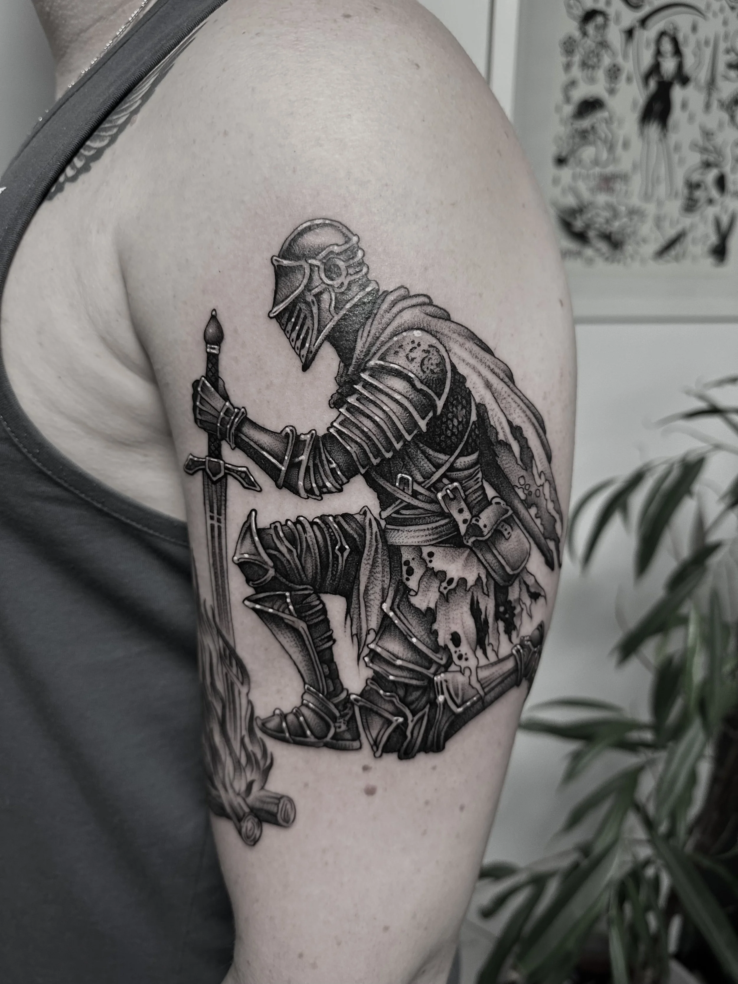 Schwarze Tätowierung eines Ritters in Rüstung, der mit einem Schwert in einer lodernden Feuerstelle kniet, auf dem Oberarm.