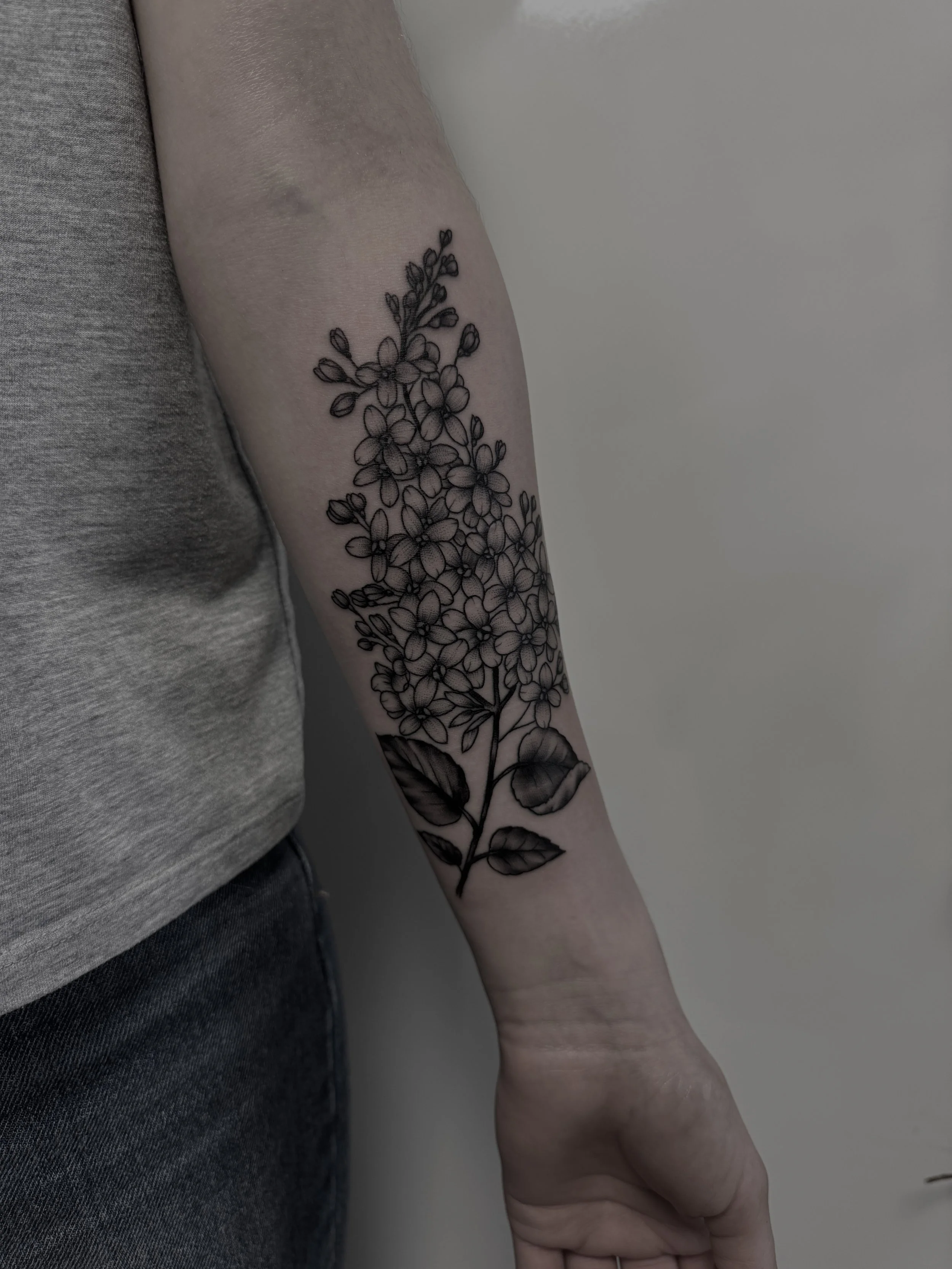 Schwarzes Blumen-Tattoo auf dem Unterarm einer Person.