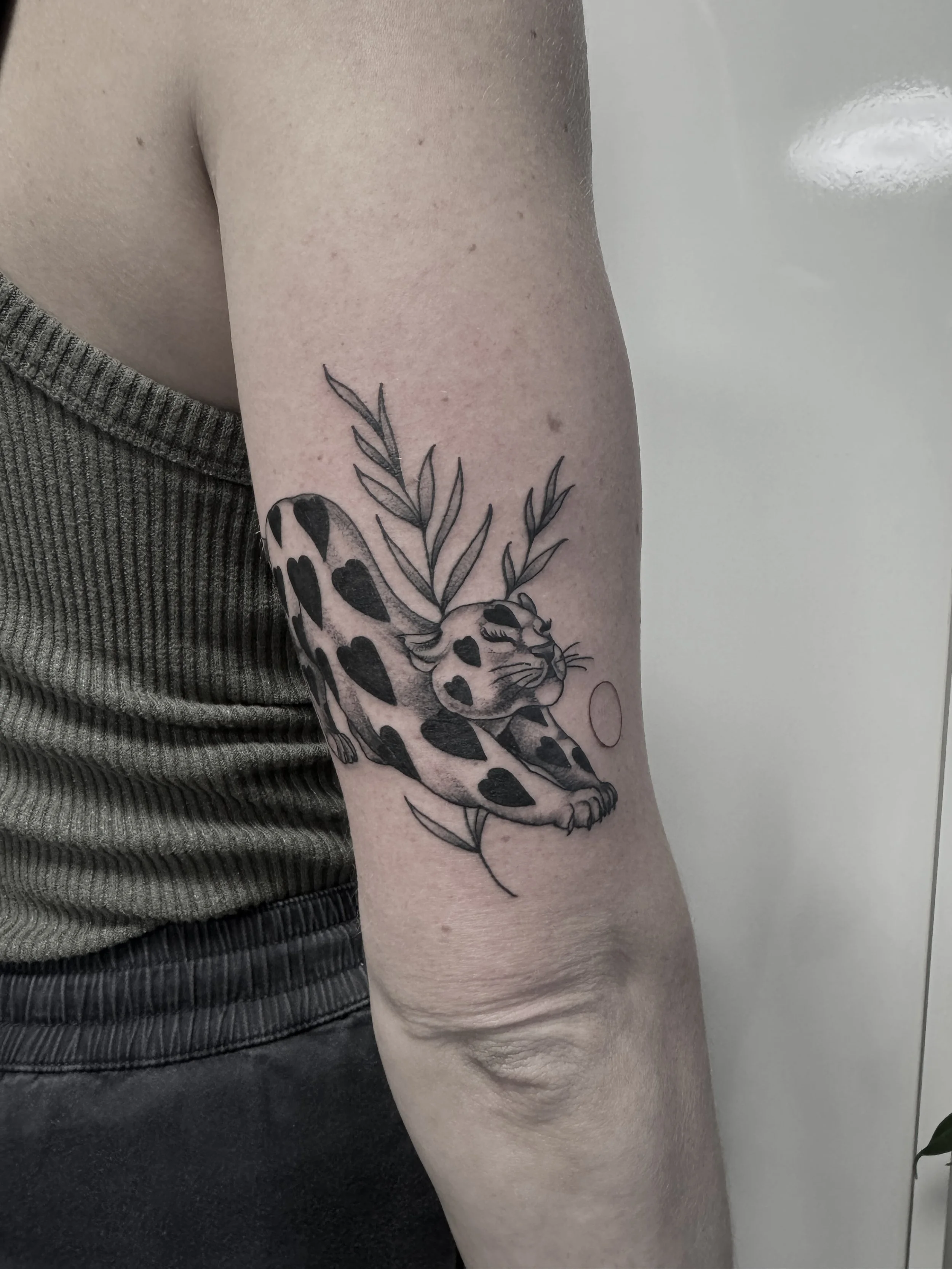 Tattoo eines Leoparden mit Herzmustern, umgeben von Blättern auf dem Oberarm.