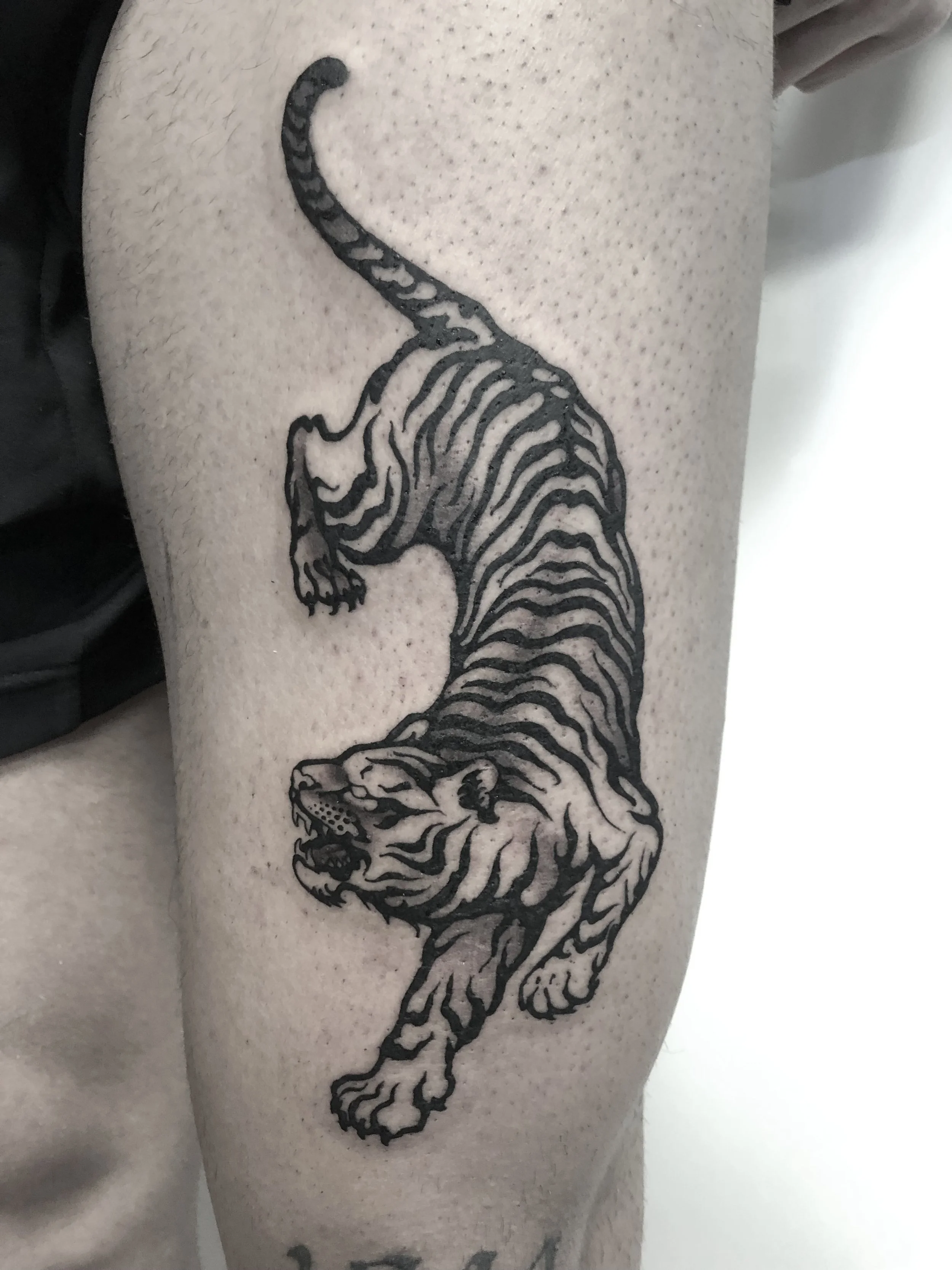 Schwarze Tätowierung eines springenden Tigers auf Haut.