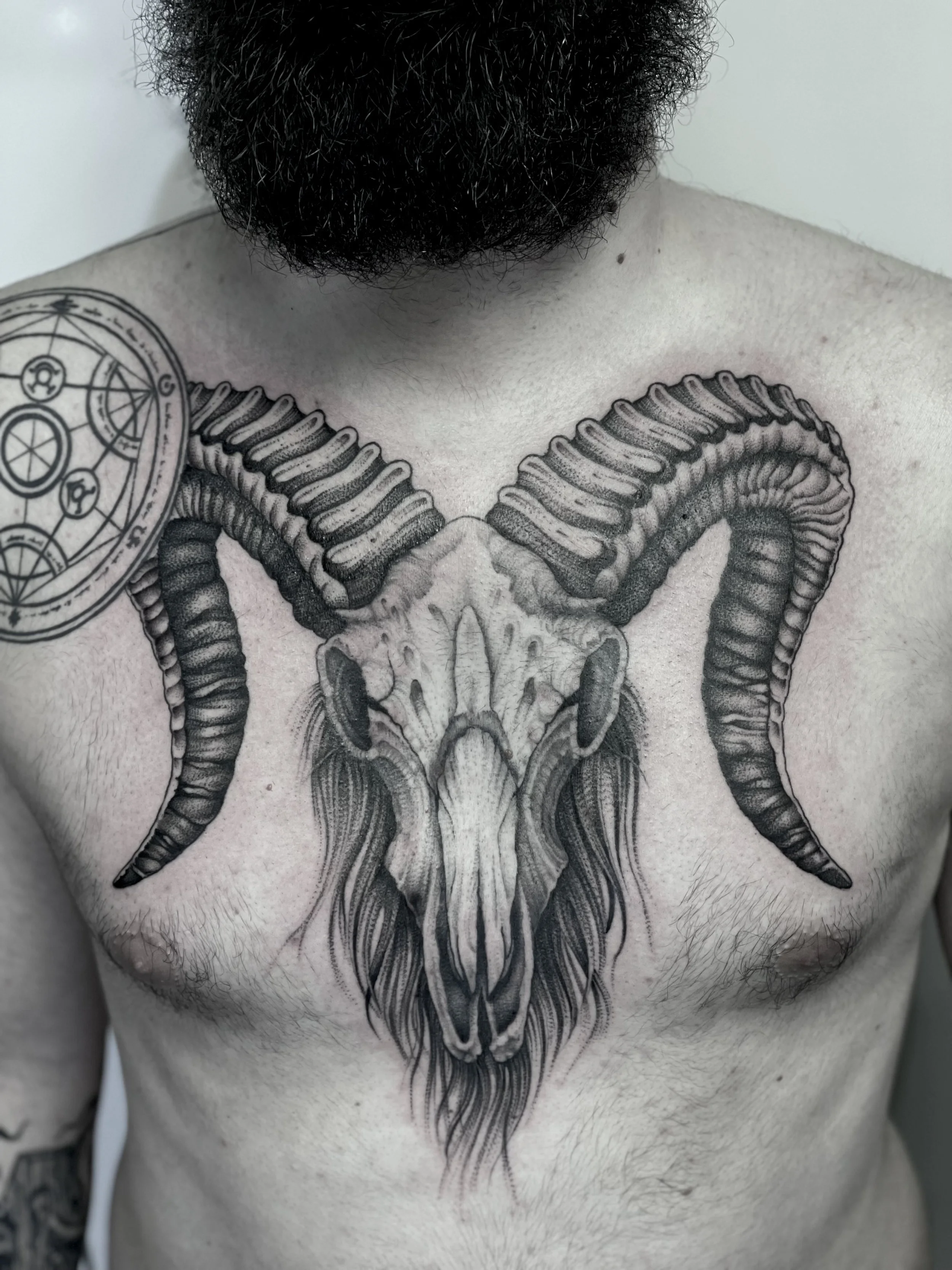 Tattogemälde eines Ziegenkopfs mit großen geschwungenen Hörnern auf der Brust eines Mannes.