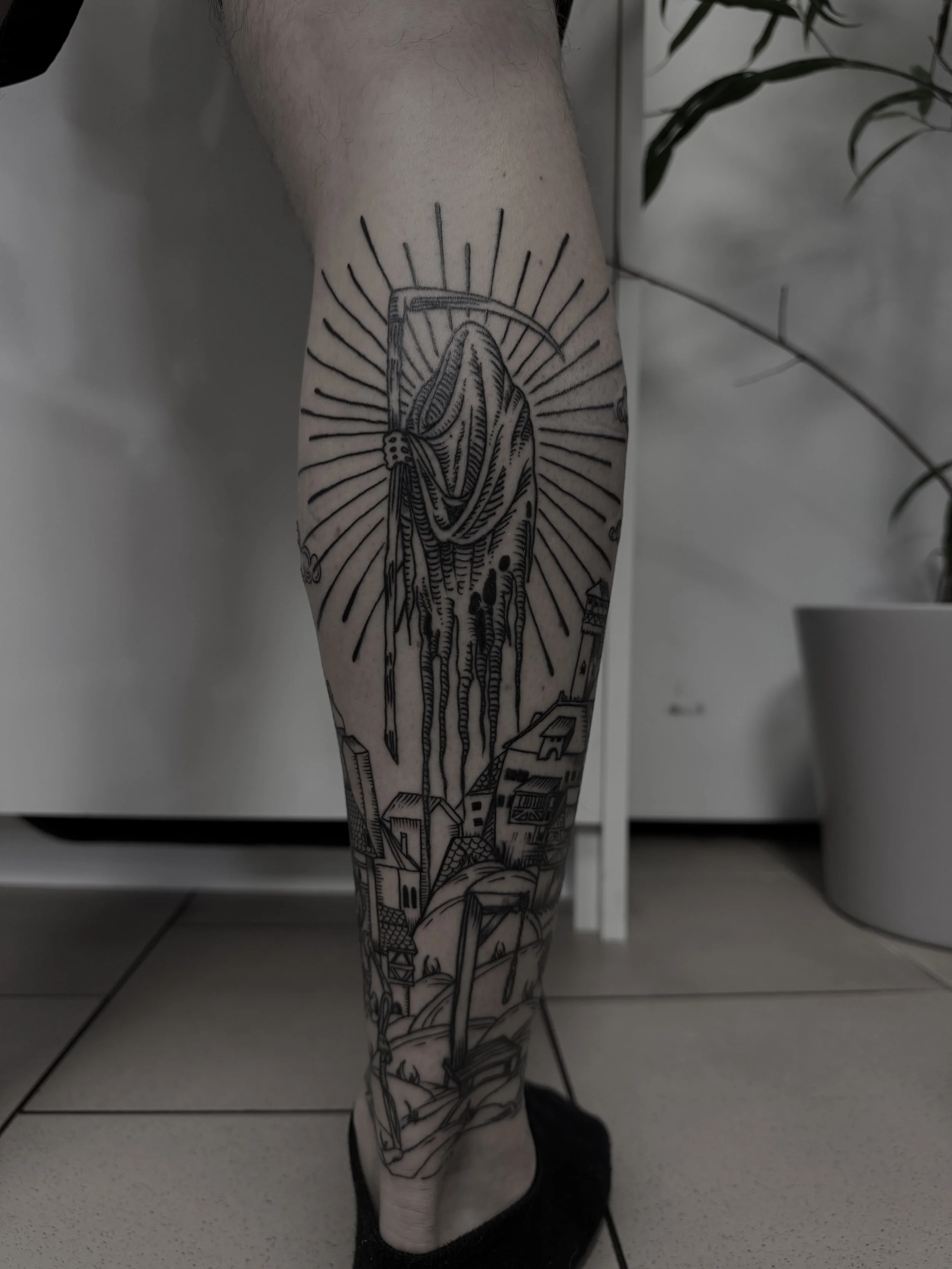 Schwarze Tätowierung auf Unterschenkel zeigt eine Landschaft mit Häusern und einer Figur, die eine kuhähnliche Kopfbedeckung trägt, umgeben von Sonnenstrahlen.