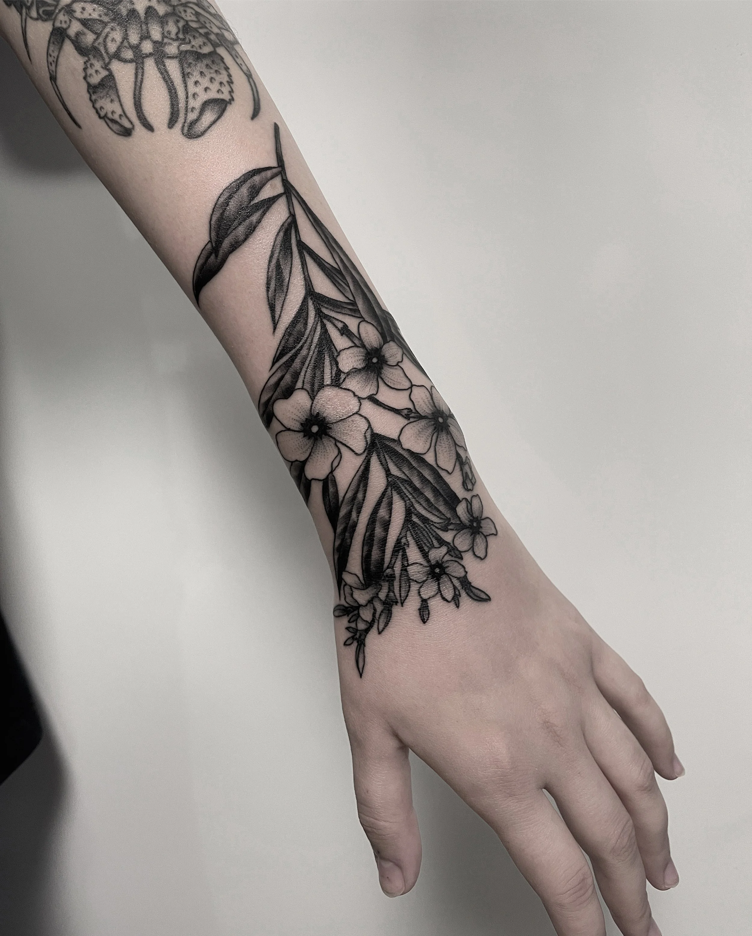 Schwarzes Tattoo eines Blumenmotivs auf dem Unterarm, bestehend aus mehreren Blüten und Blättern.