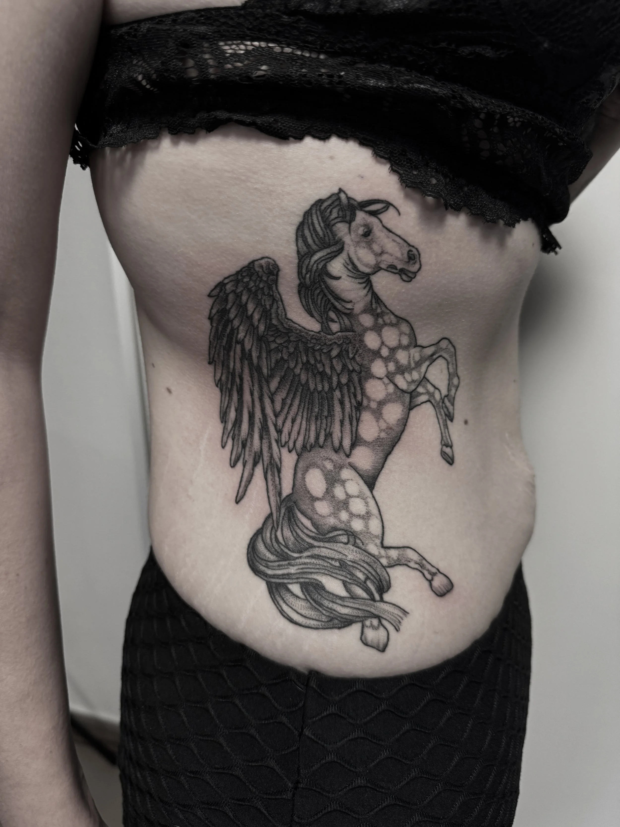 Tattoo eines geflügelten Einhorns auf dem Rippenbereich einer Person.