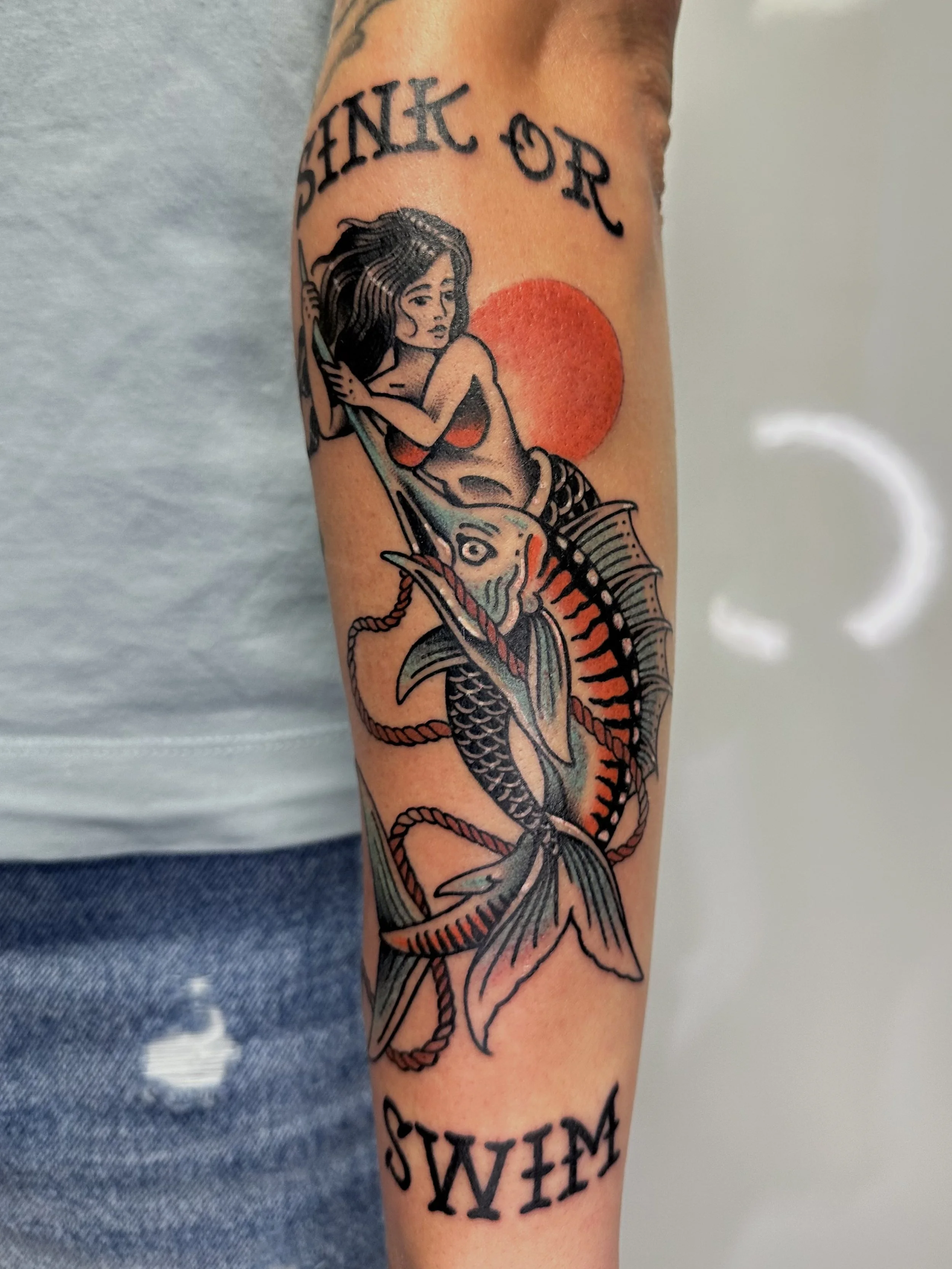 Tätowierung eines Mädchens auf einem Fisch mit Sonnenuntergang im Hintergrund und der deutschen Worte 'Denke oder Schwimm'.