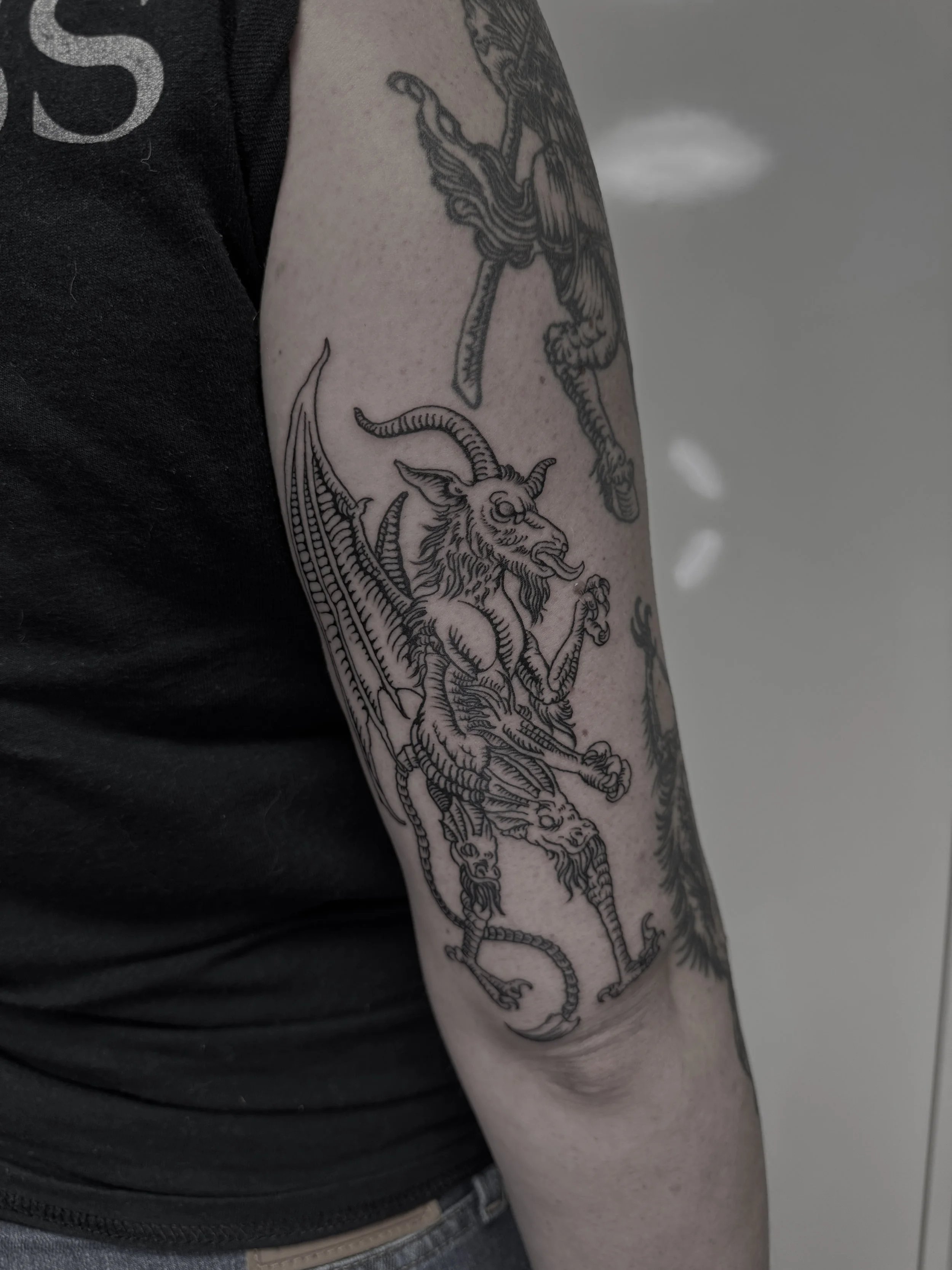 Schwarze Tätowierung eines dämonischen Drachen auf dem Oberarm einer Person.