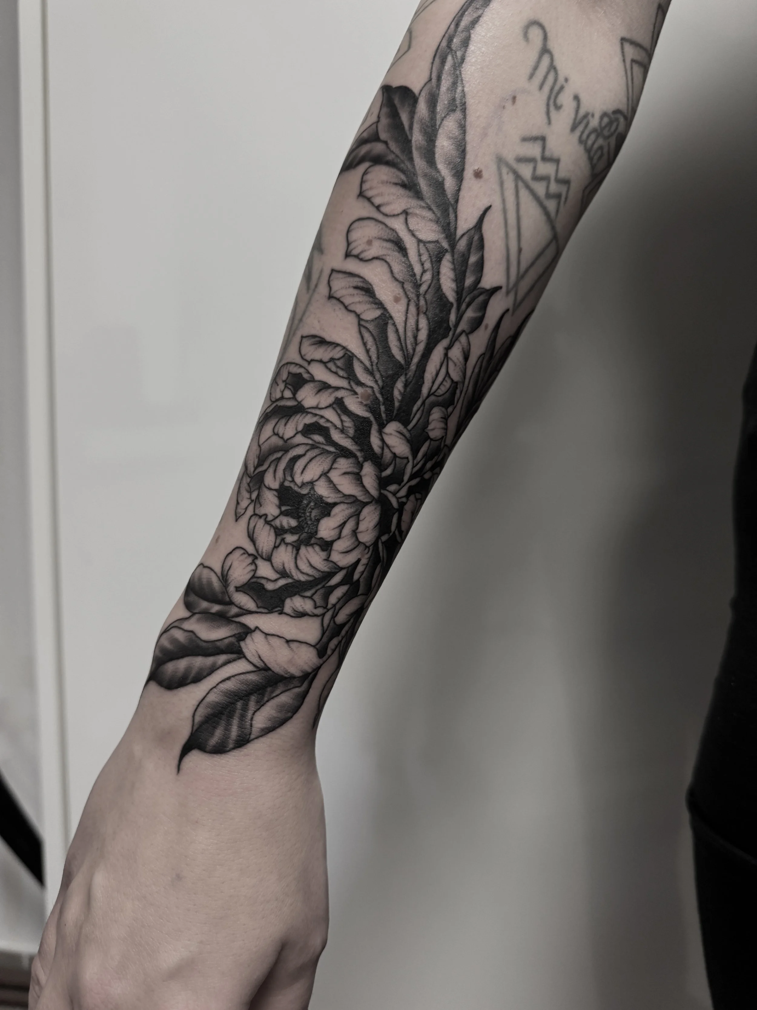 Schwarze und graue Tätowierung eines großen Blumenmusters auf dem Unterarm.