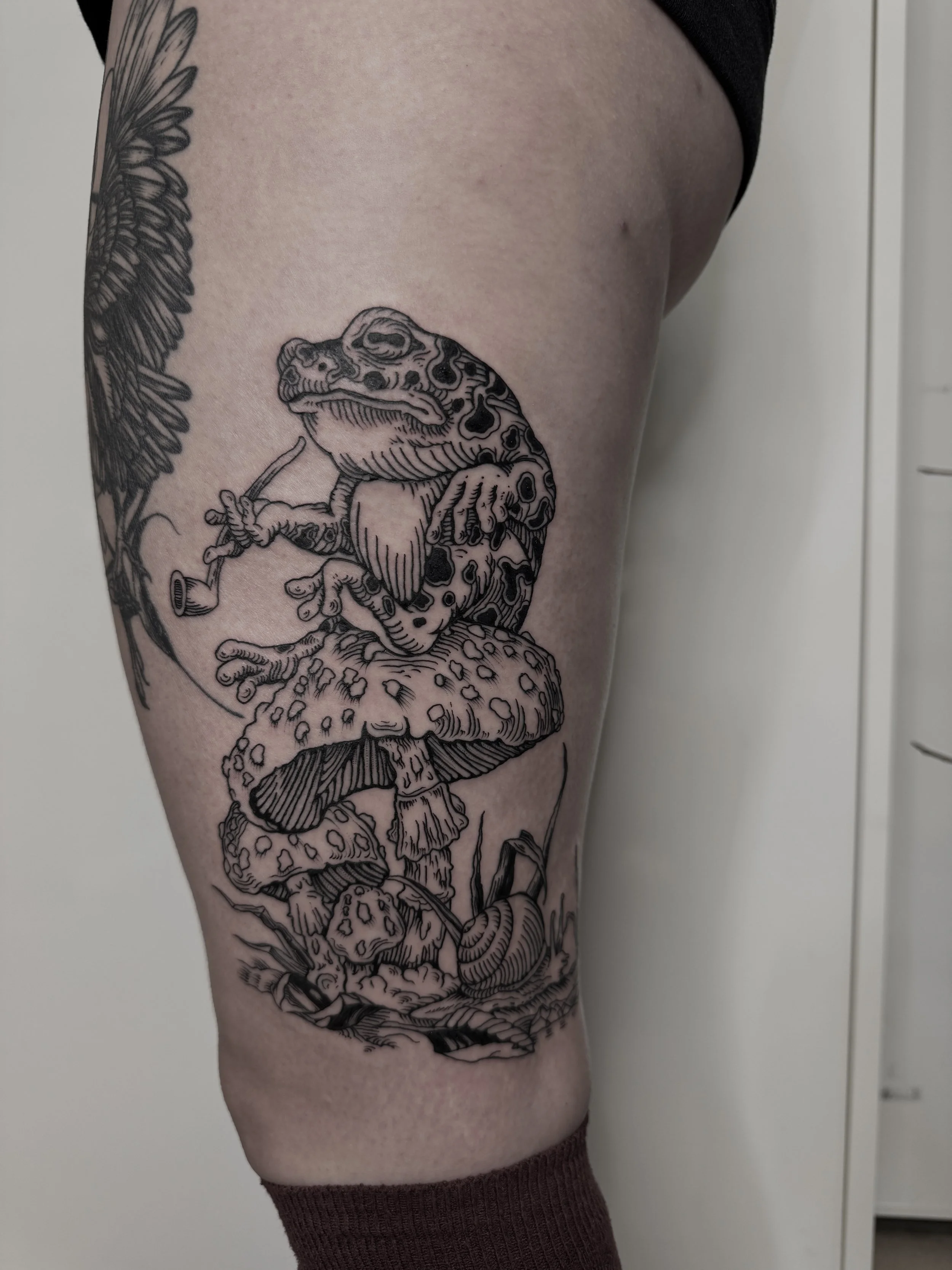 Tattoo auf Oberschenkel mit einem Gecko, einer giftigen Pilztoadstool und Schnecken, alle in schwarzer Linienzeichnung.