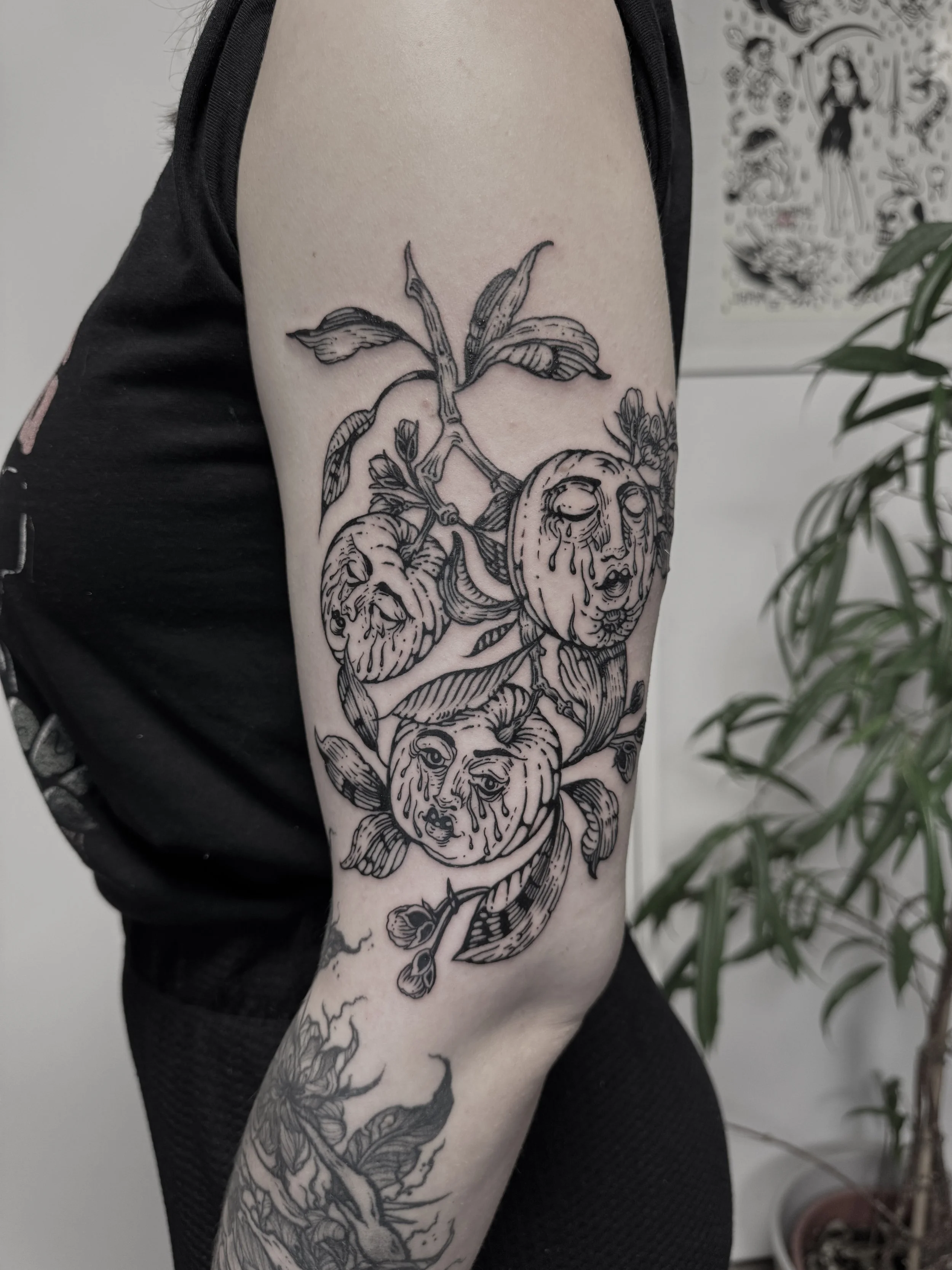 Tattoo an einem Arm mit einem Pflanzendetail und mehreren lächelnden Fruchtköpfen, die Tränen vergießen.