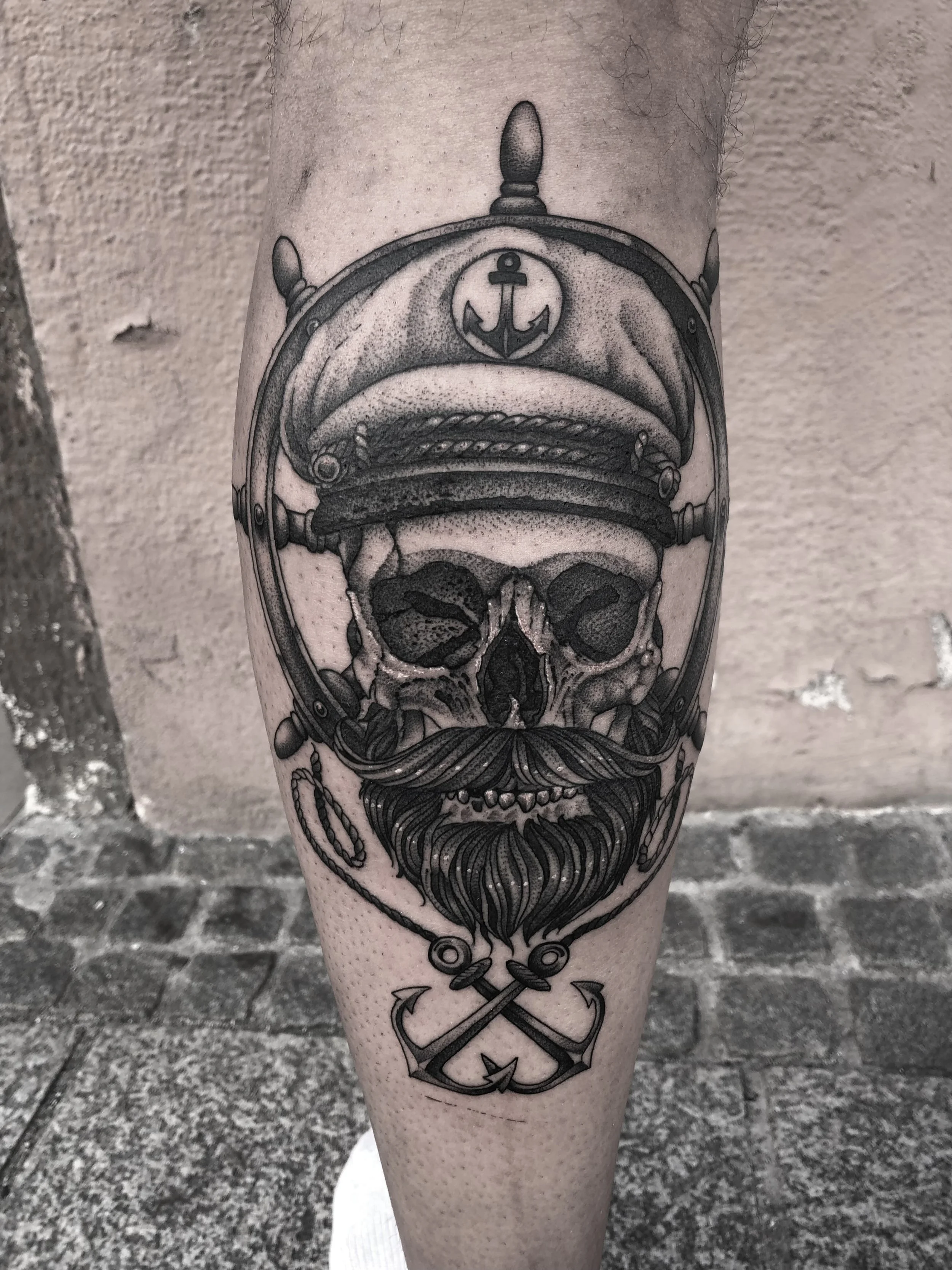 Tattoo eines Schädels mit Muschel, Anker und Seemannsmütze auf einem Bein.