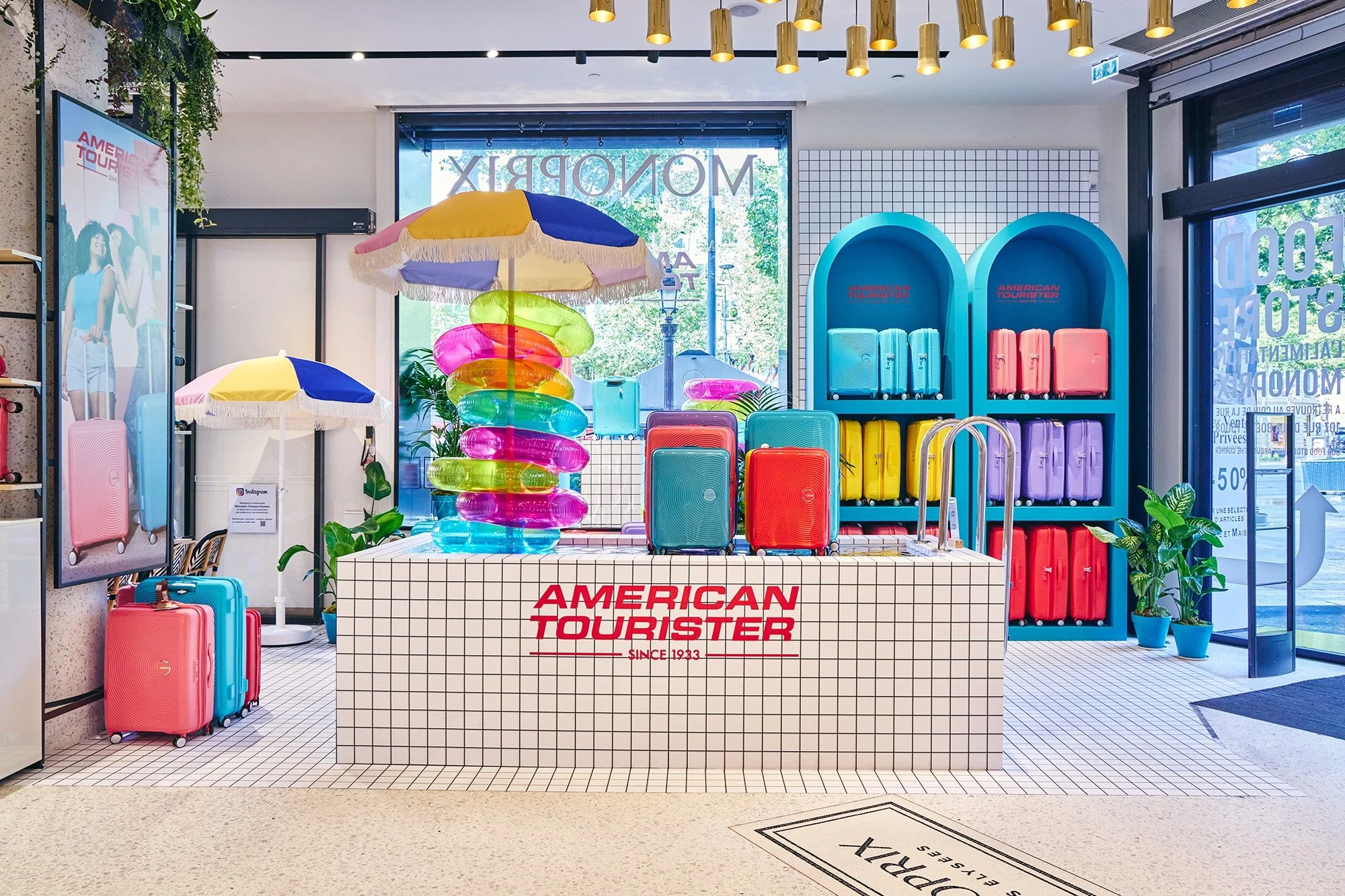 Vitrine de souvenirs de voyage colorés avec valises, parasols, et accessoires, dans un magasin de la marque American Tourister.