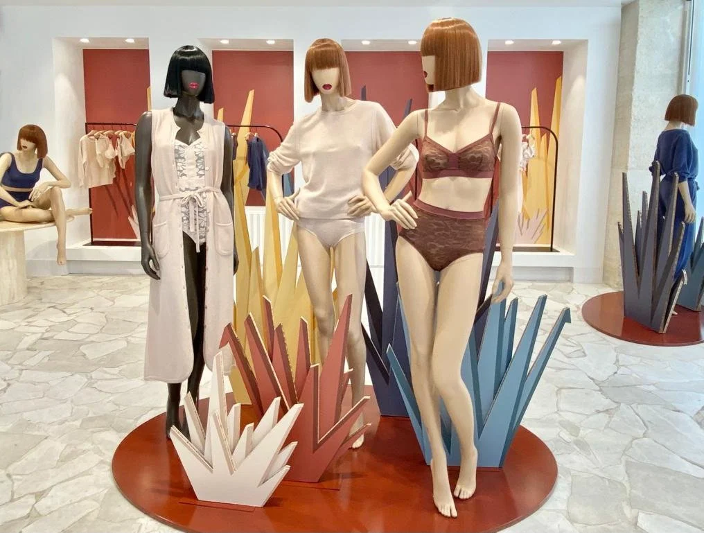 Mannequins portant des vêtements d'été et de lingerie dans une vitrine de magasin avec décor de formes géométriques colorées.