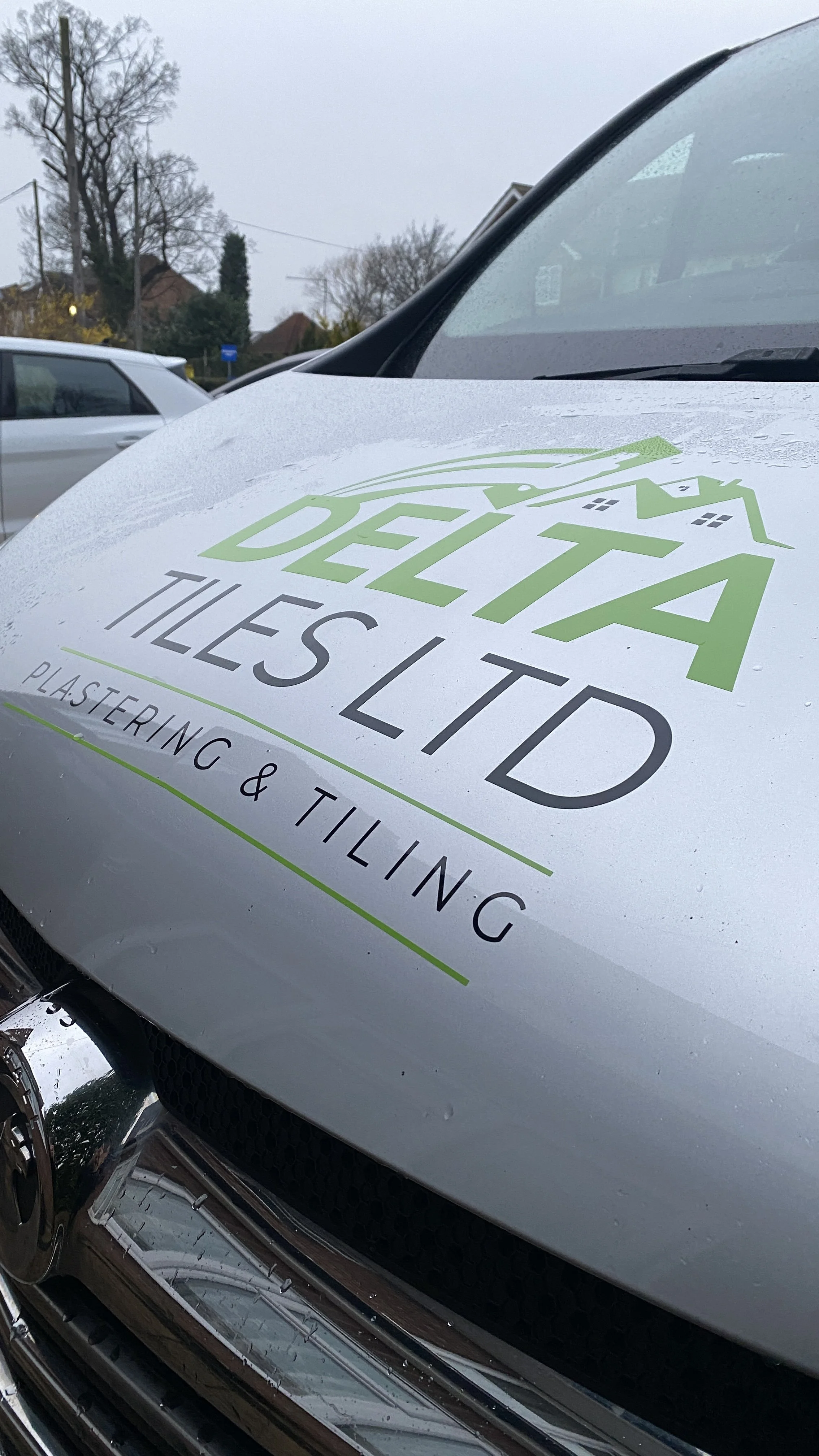 Close-up of a vehicle with a decal that says 'Data Deltd Tiles Ltd' and mentions plastering and tiling services.