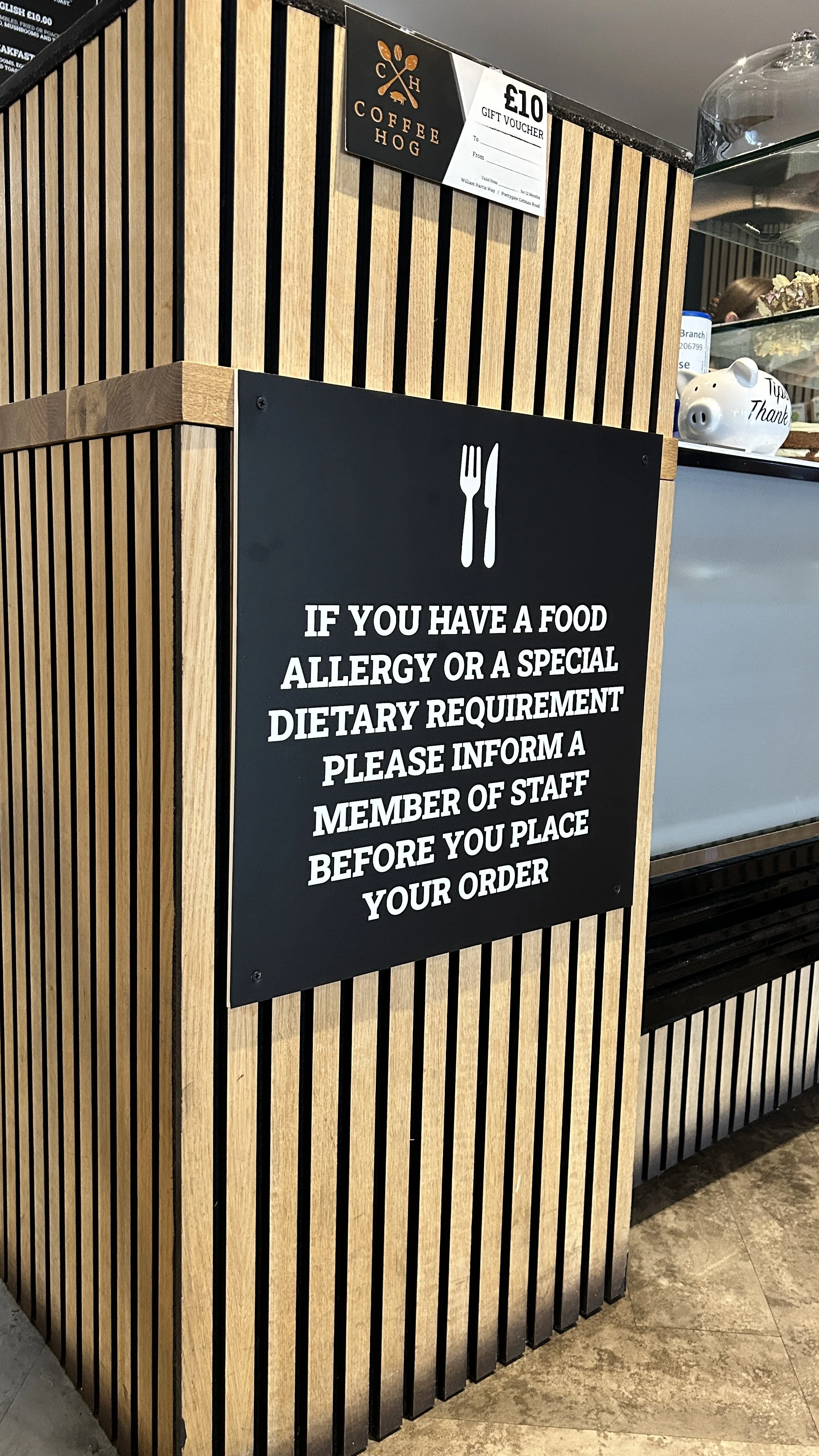 Sign at a restaurant with a fork and knife icon, instructing customers with food allergies or special dietary needs to inform staff before ordering.