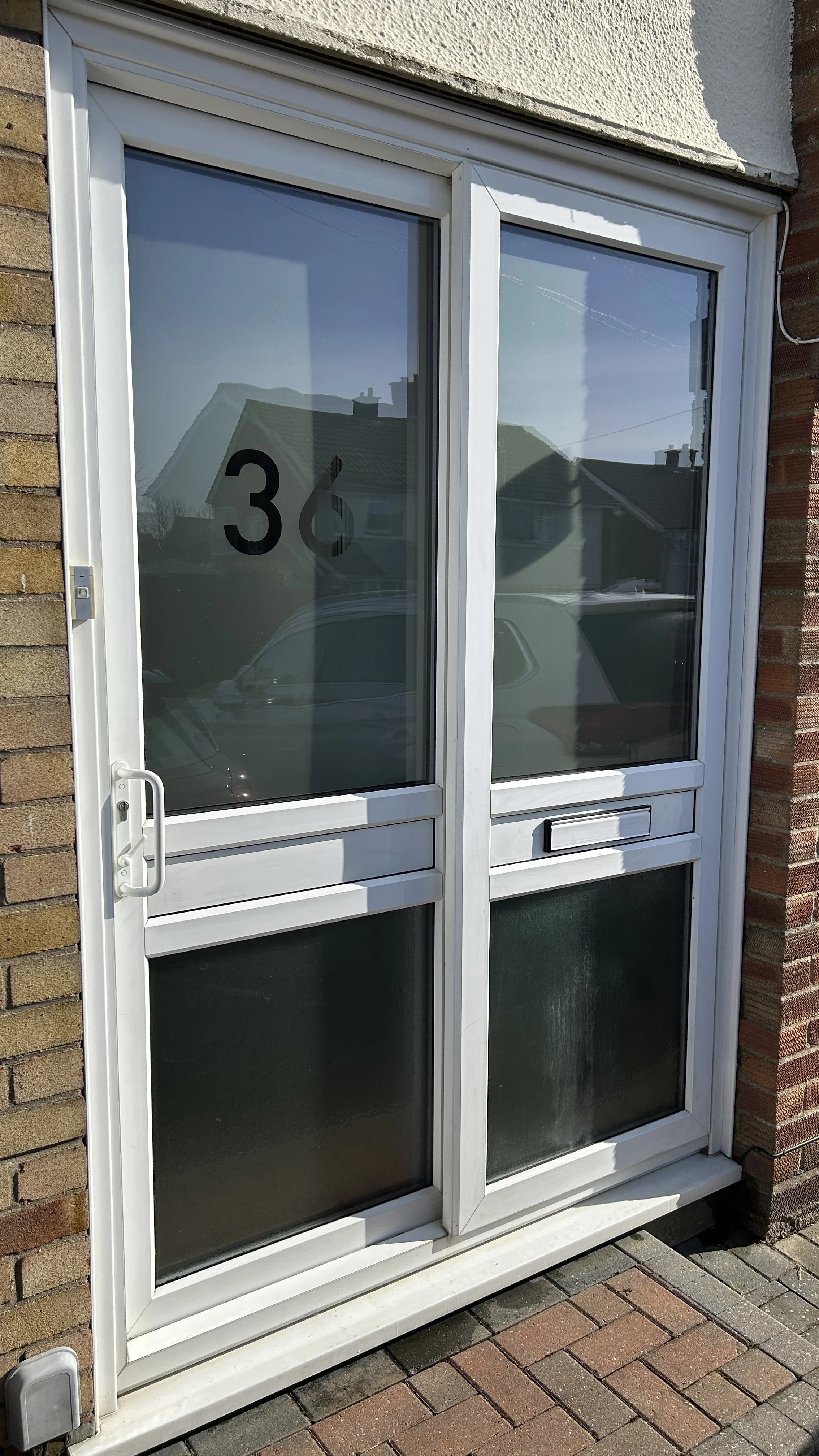 Glass door with house number 36, framed in white, with a brick wall on the right side and a brick sidewalk in front.