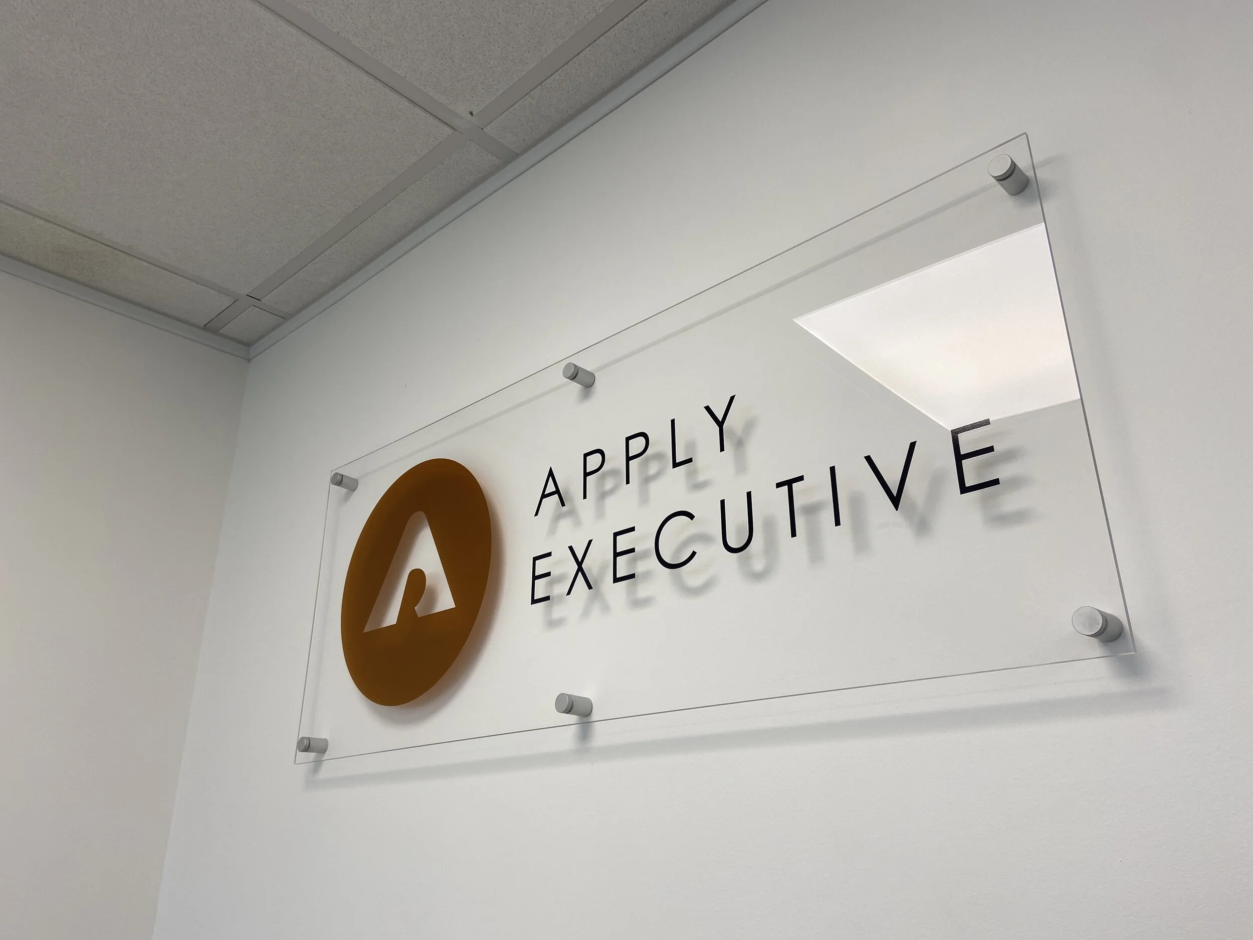 Office sign with a gold logo and the words 'APPLY EXECUTIVE' on white wall.