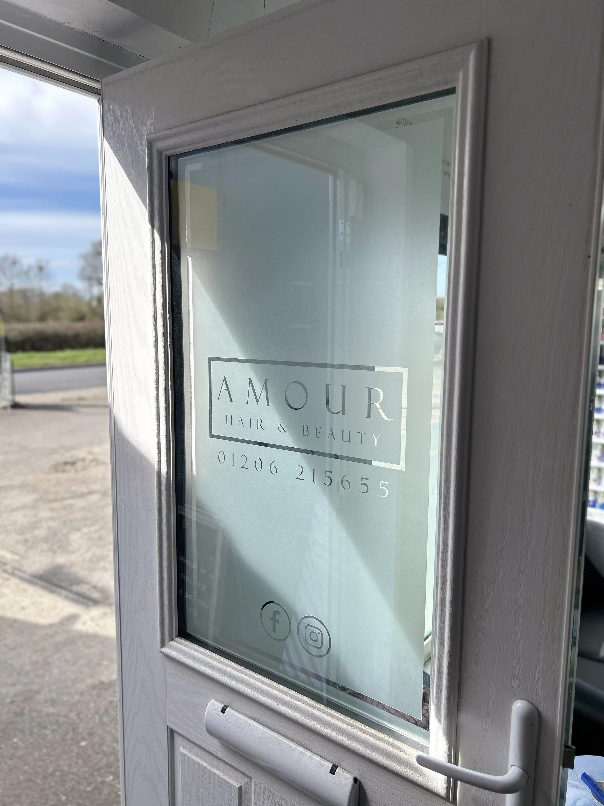 A vending kiosk with a sign for Amour Hair & Beauty, displaying social media icons for Facebook and Instagram, with a scenic outdoor background including trees and a cloudy sky.
